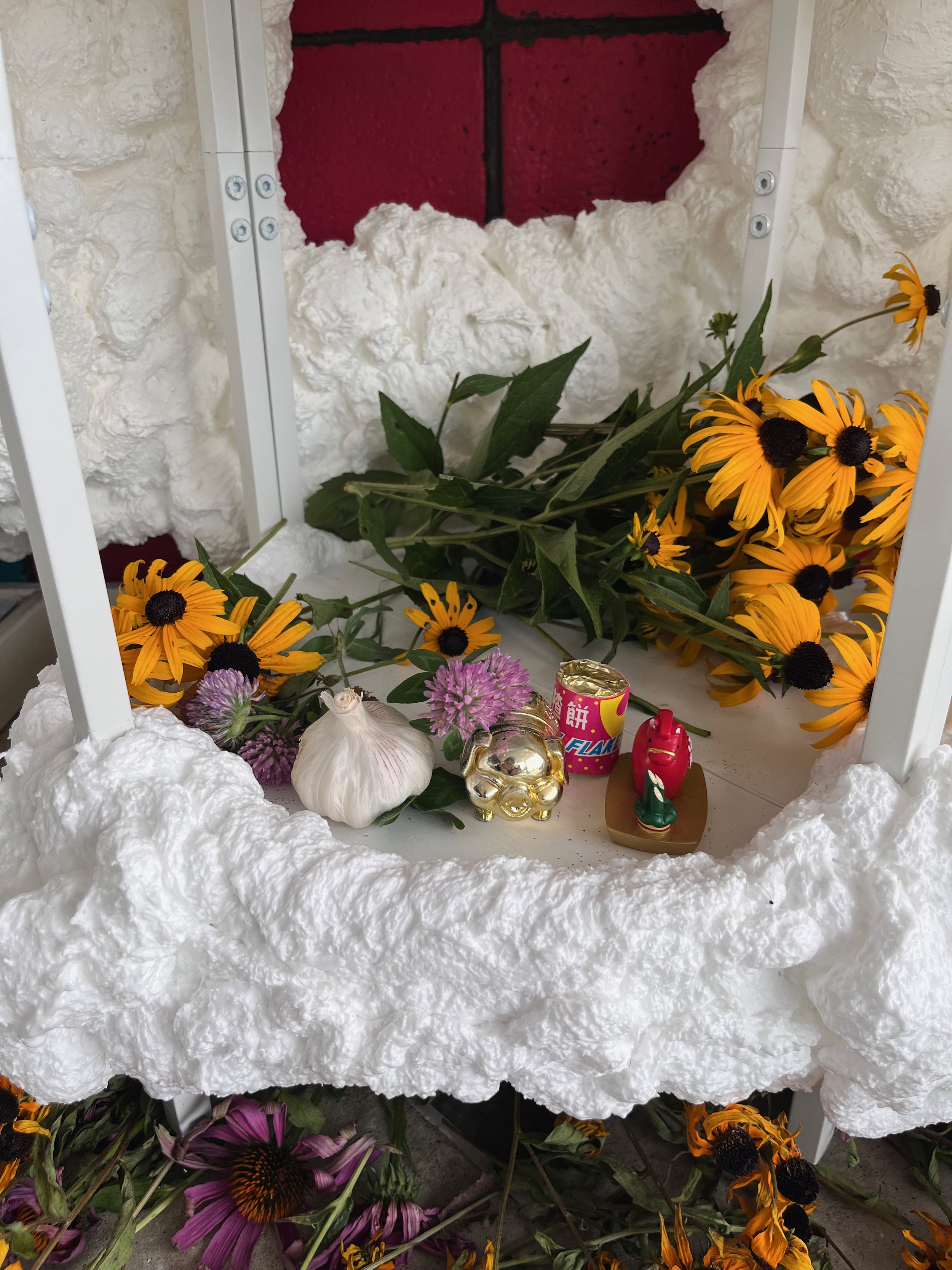 An altar space holds flowers, garlic, candy, and small statues