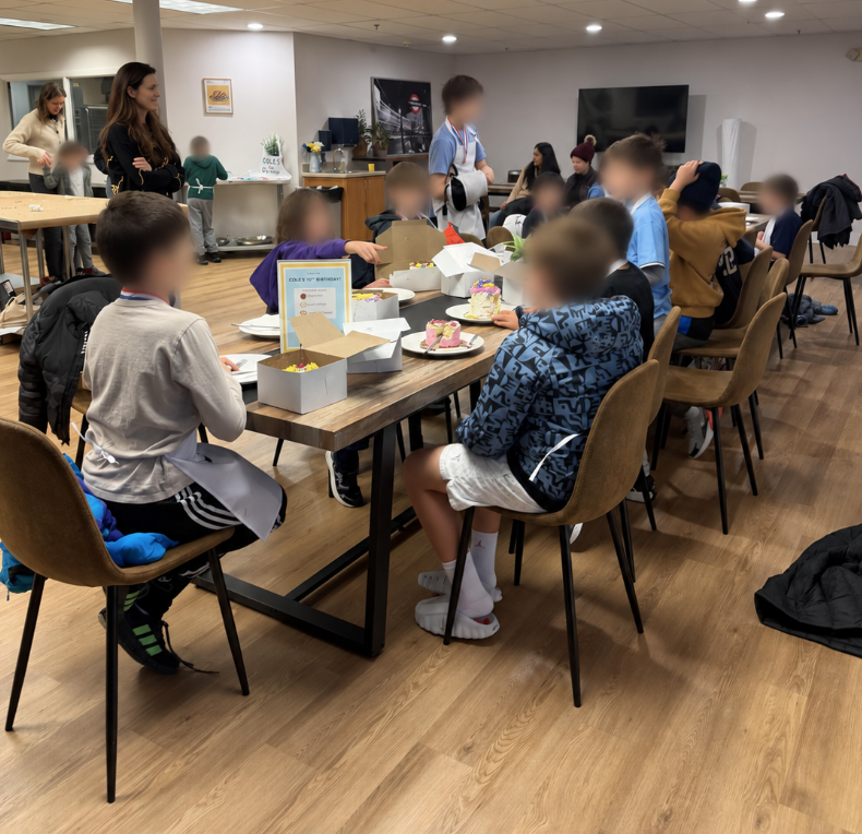 Kids sat at a birthday table with cake and aprons on.