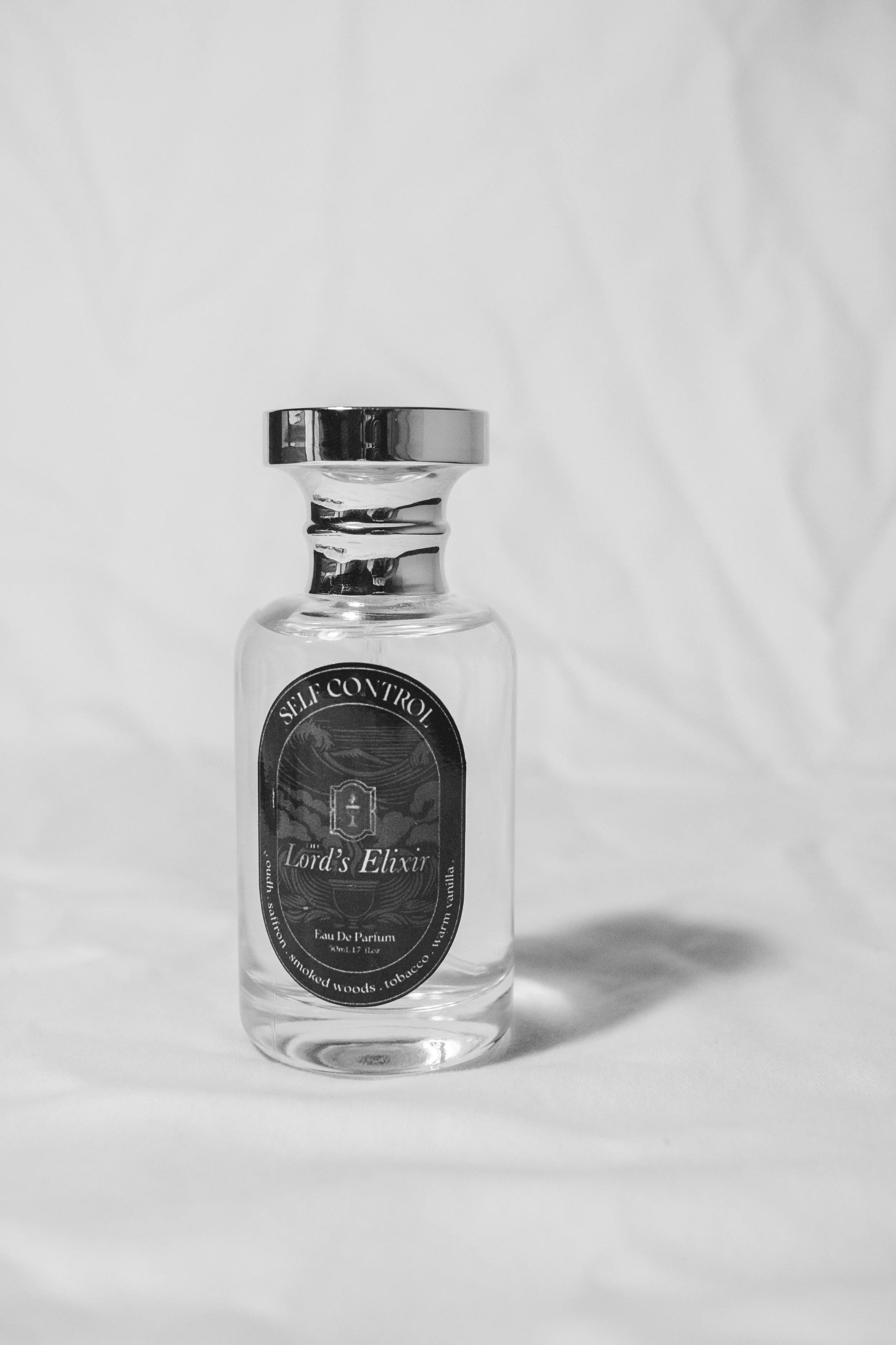 A clear glass perfume bottle labeled 'Lord's Elixir,' standing on a plain white background.