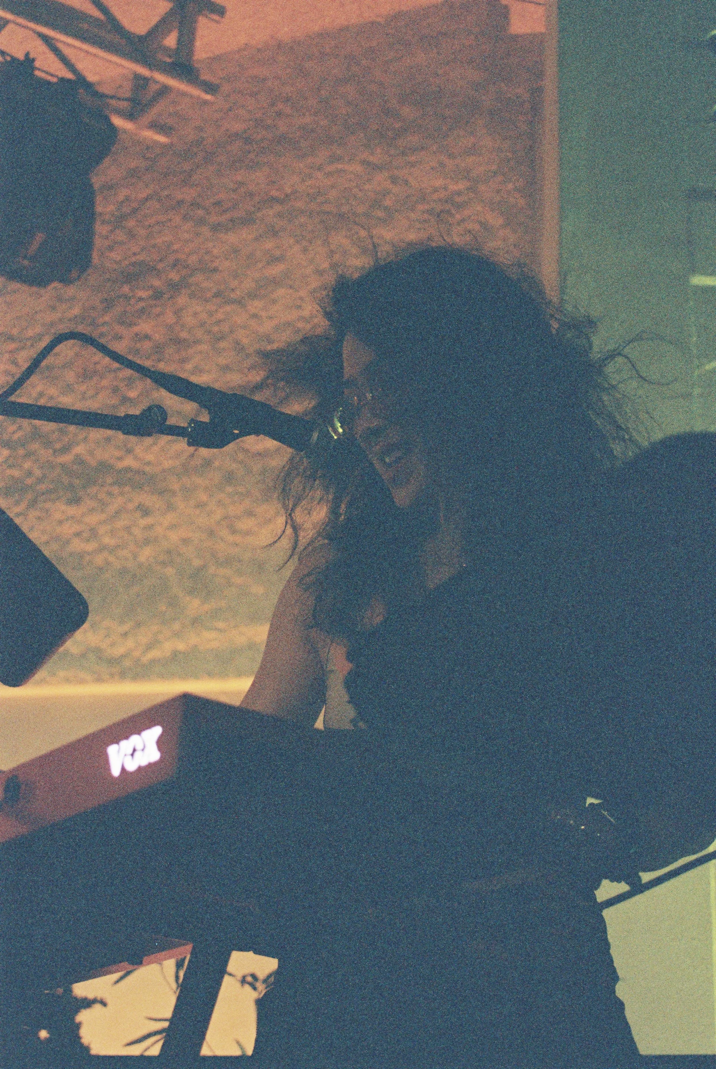 A person with dark, curly hair is visible in the foreground, holding what appears to be a microphone while playing the keyboard.