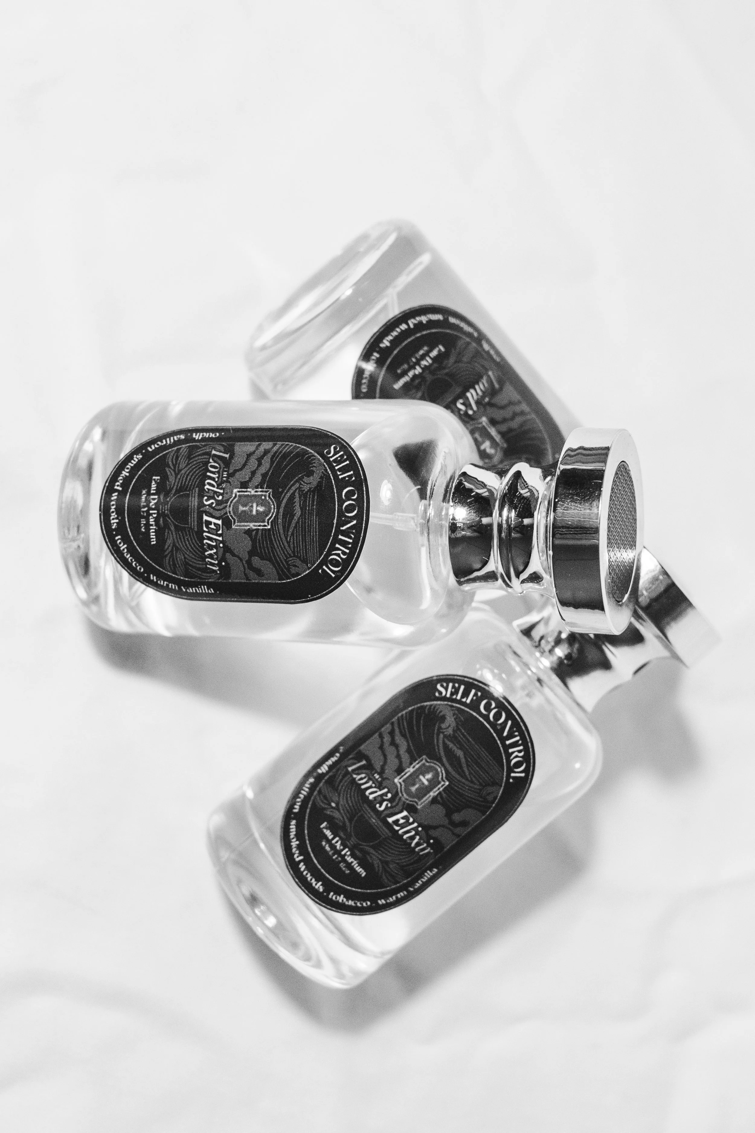 Three transparent glass perfume bottles with labels and caps lying on a white surface