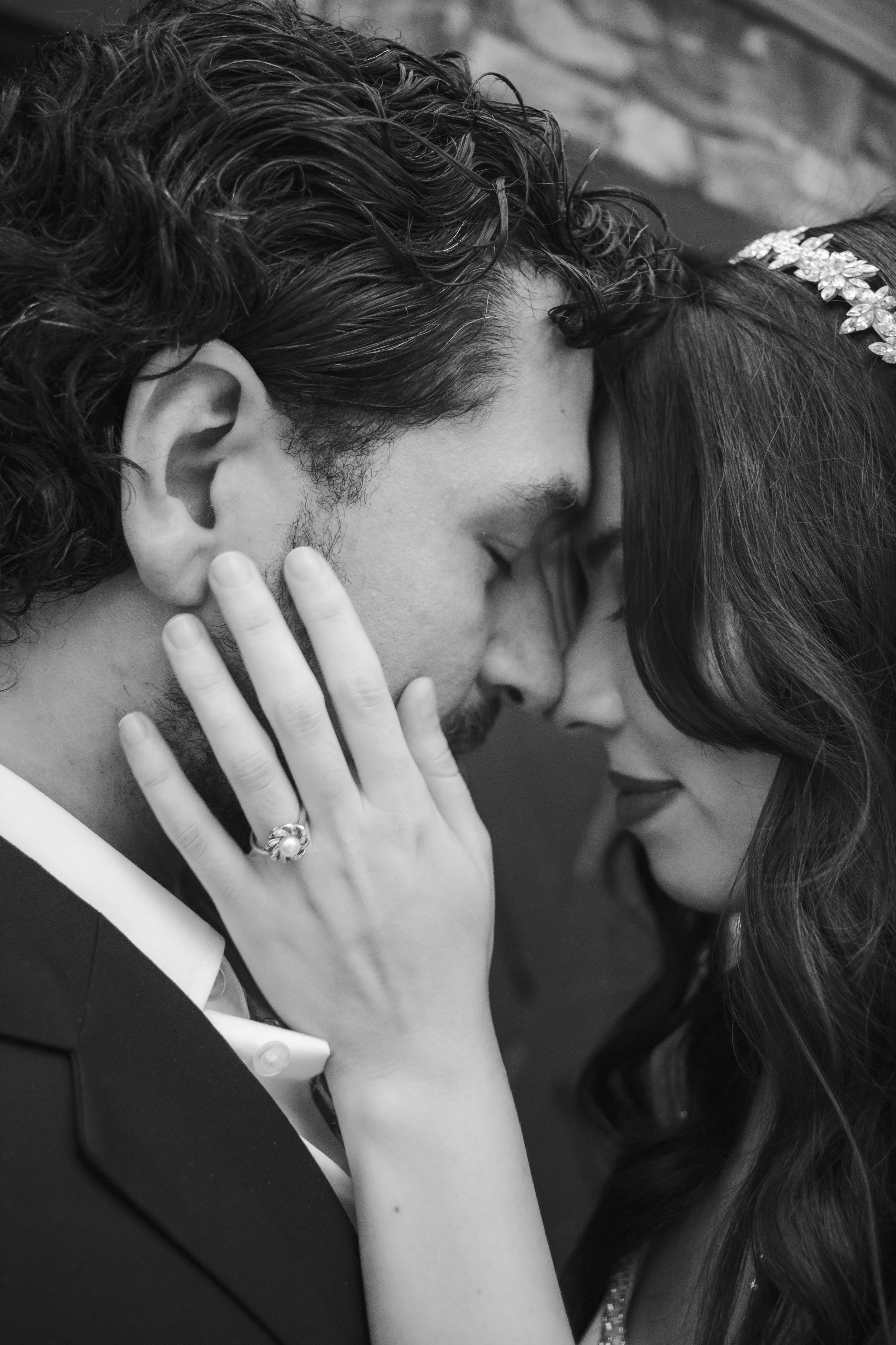 A black-and-white photograph of a couple touching foreheads and closing their eyes, appearing intimate and tender.