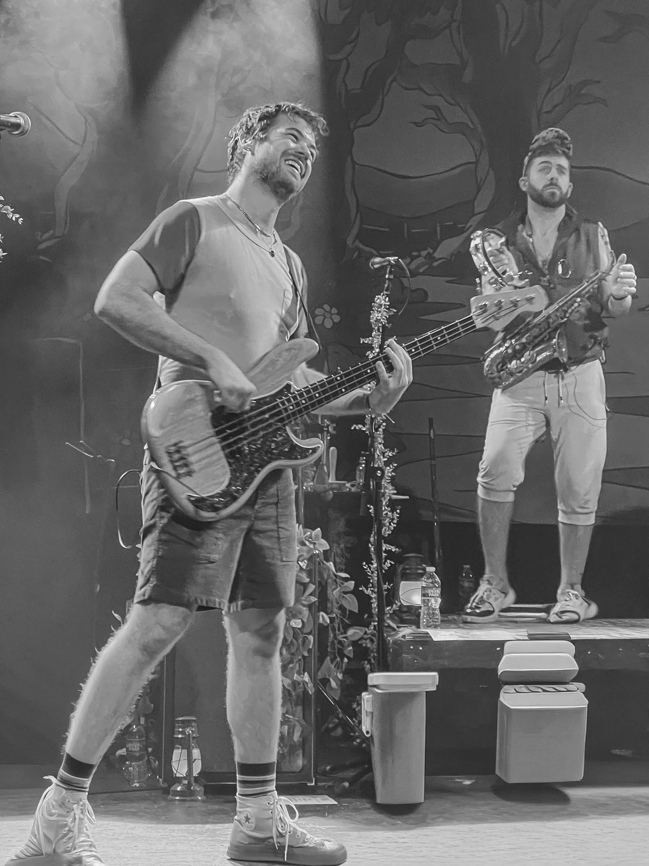 Two musicians on stage, one playing a bass guitar and the other holding a saxophone.