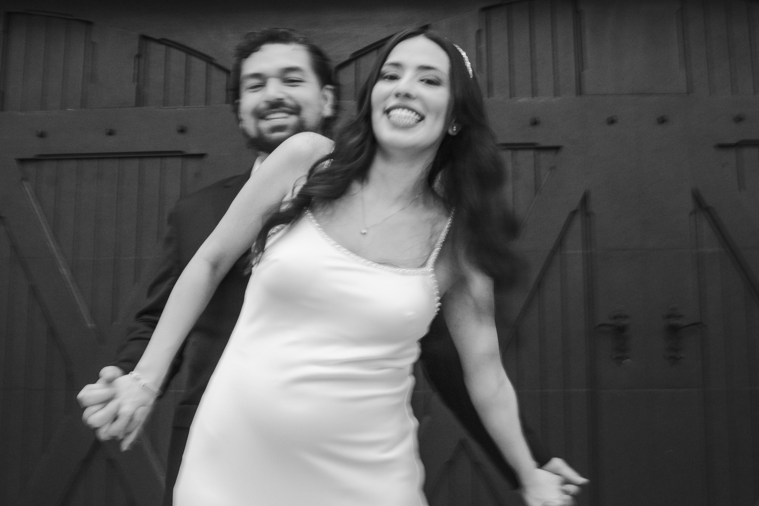 A smiling woman in a sleeveless dress and a man in a suit standing close together, holding hands in a staircase setting.