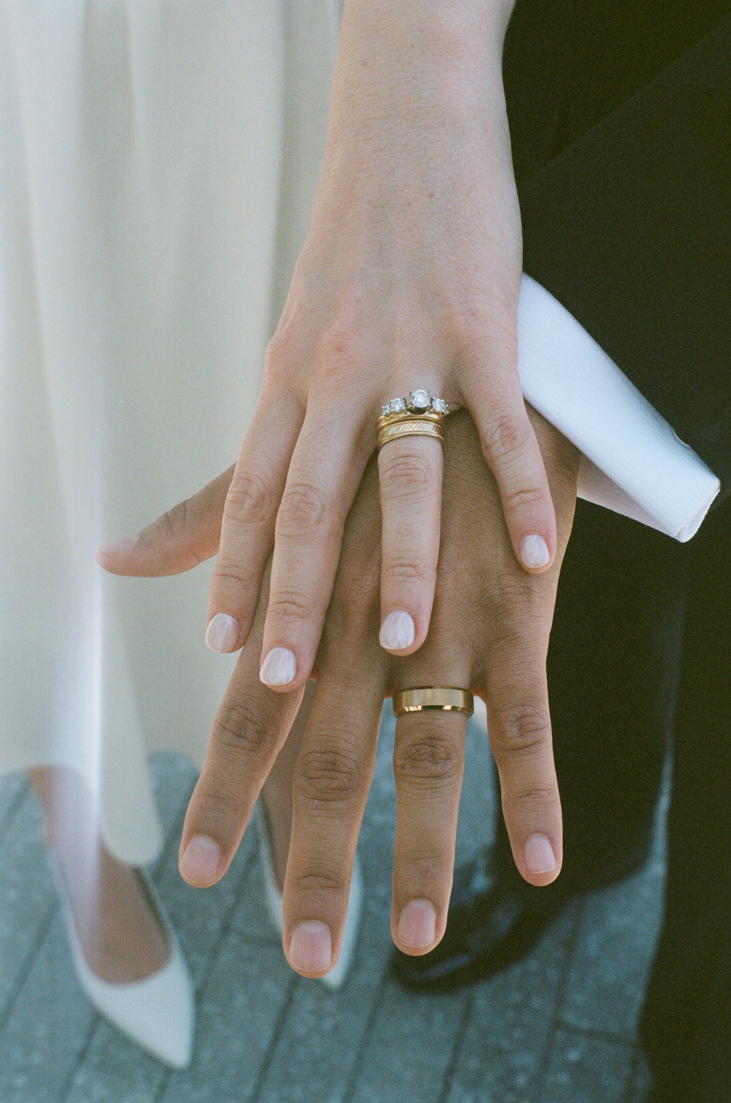 Close-up of multiple hands interlocked, showing rings on fingers, against a neutral background.