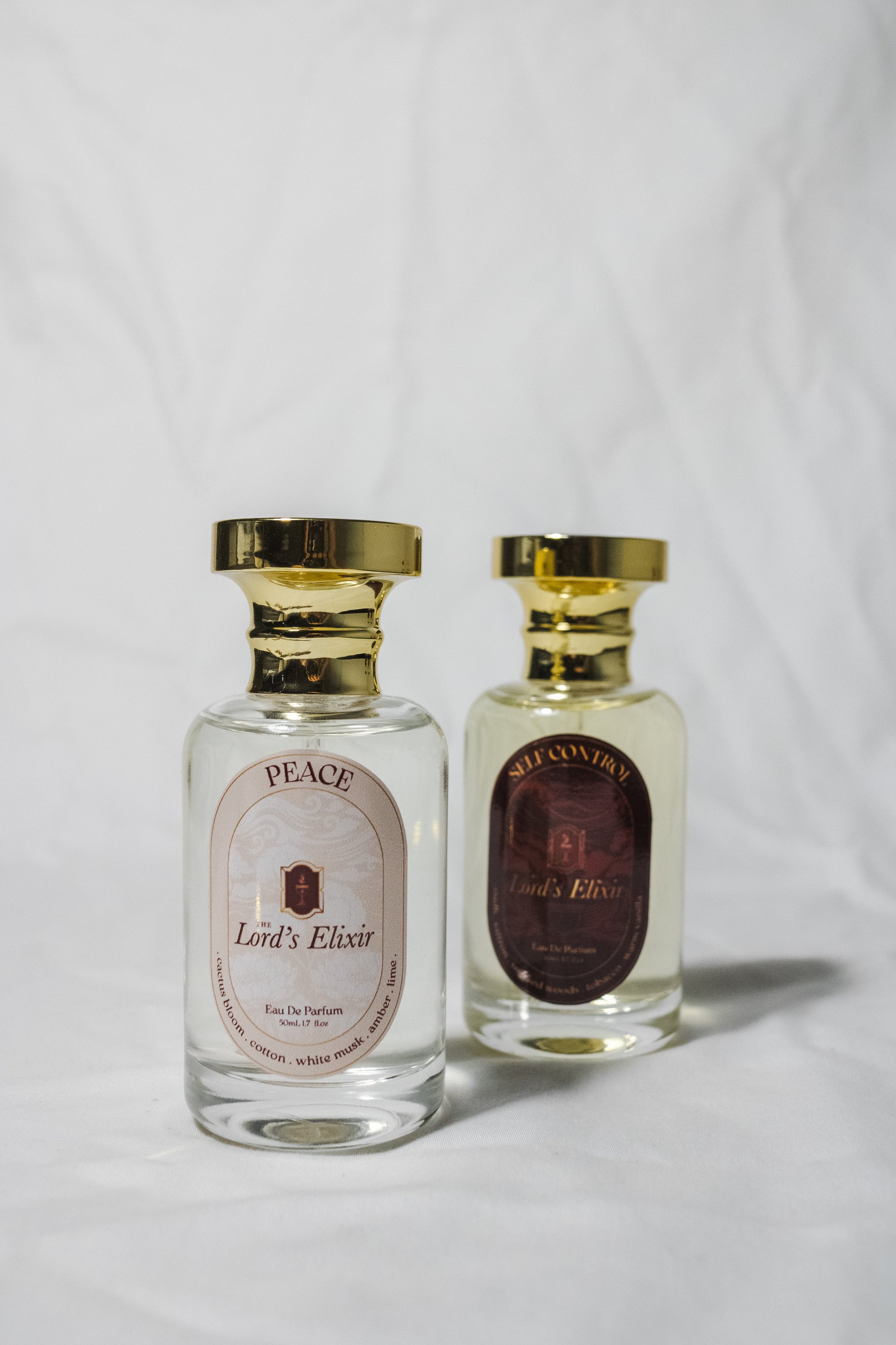Two small bottles of perfume with gold caps on a white surface against a white background