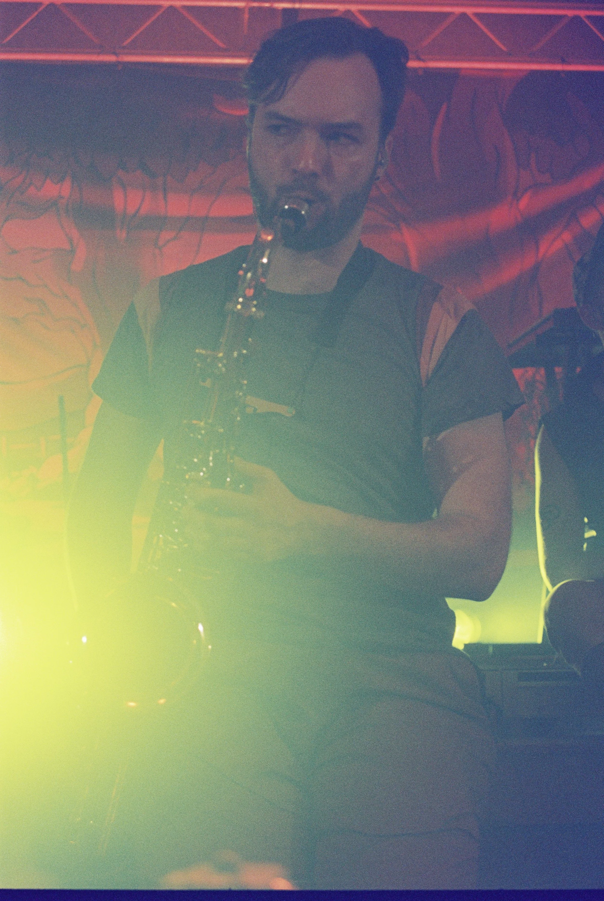 A man with a beard playing a saxophone on stage, with colorful stage lighting.