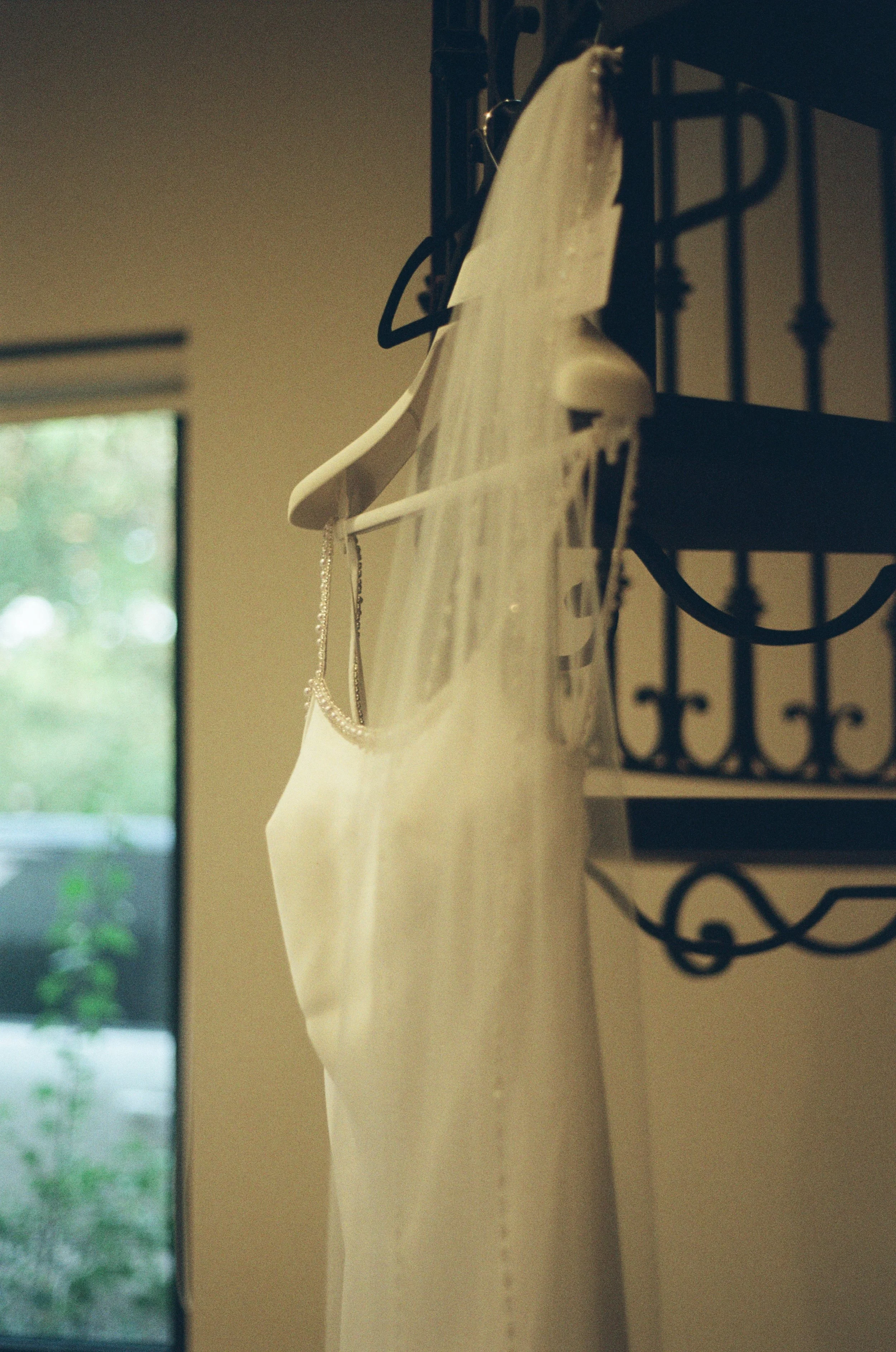 A wedding dress hanging on a black hanger inside with a window in the background.