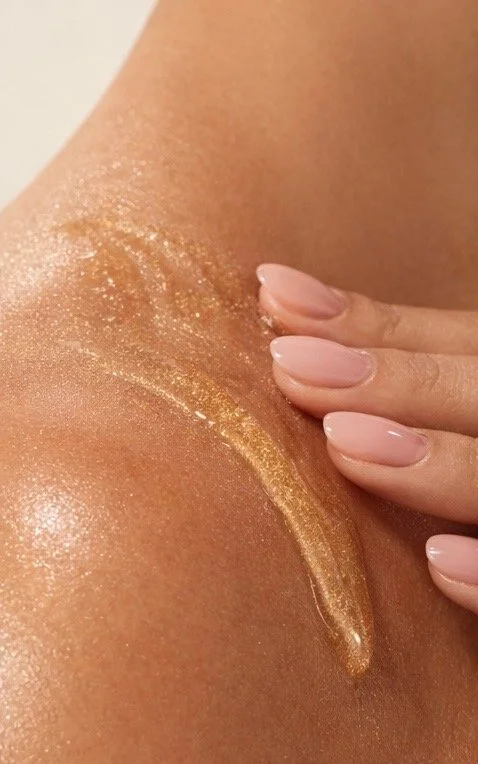 A person's arm with a streak of gold metallic body paint and smooth, manicured fingernails touching the skin.