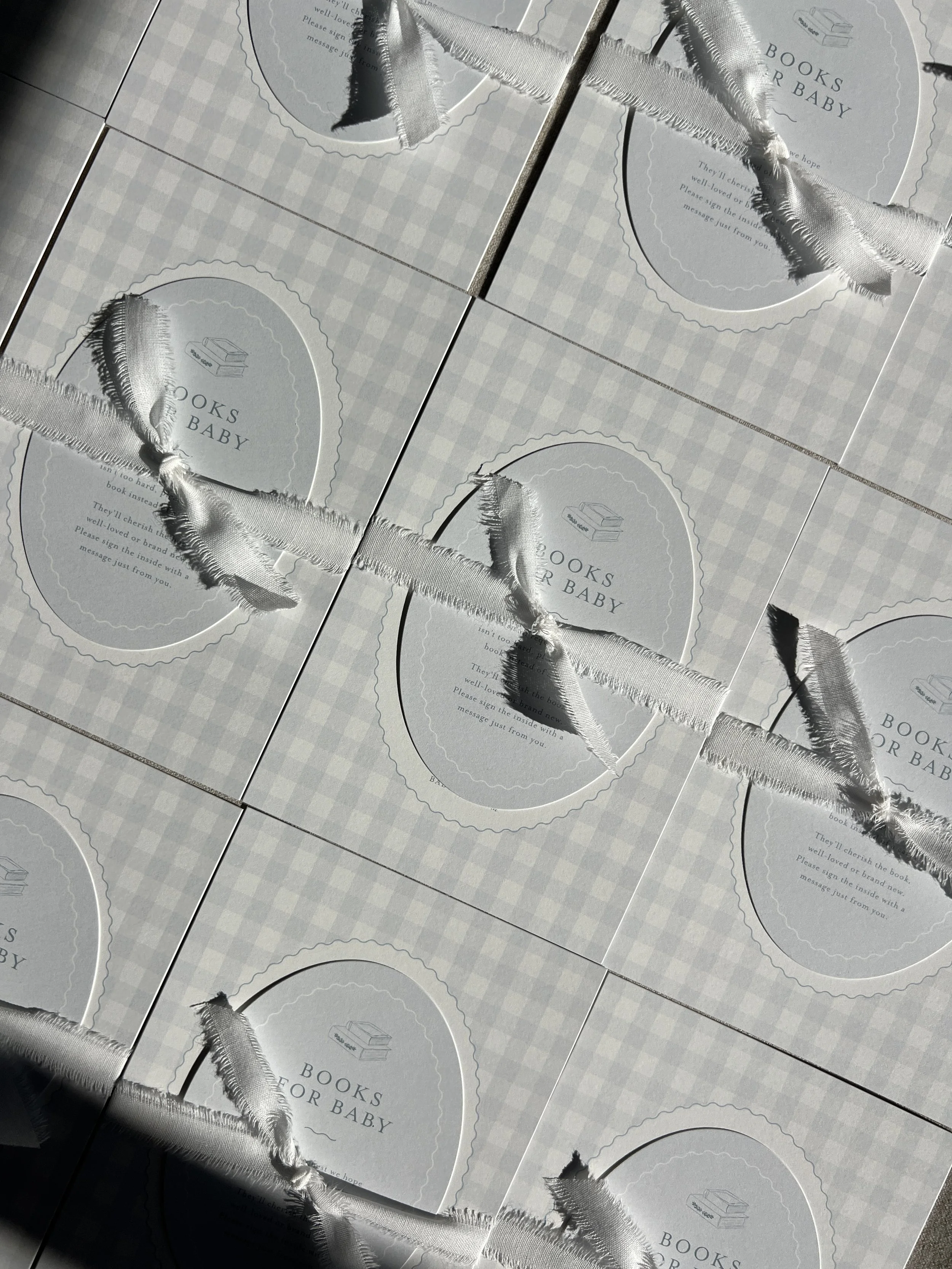 Multiple white boxes with light gray checkered pattern, labeled 'Books for Baby,' decorated with ruffled satin ribbons.