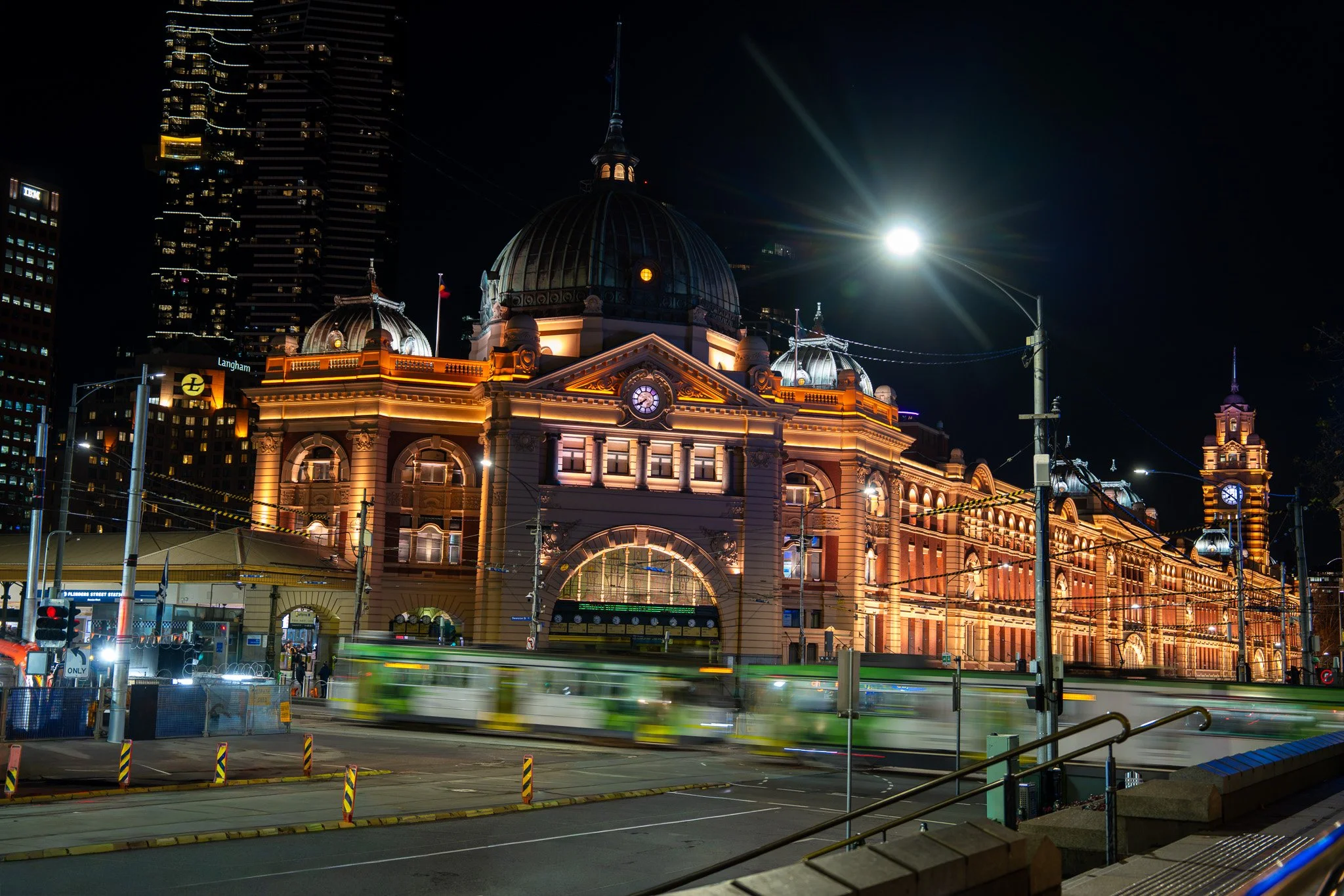 Flinders Street Station at night with trams crossing in front of it