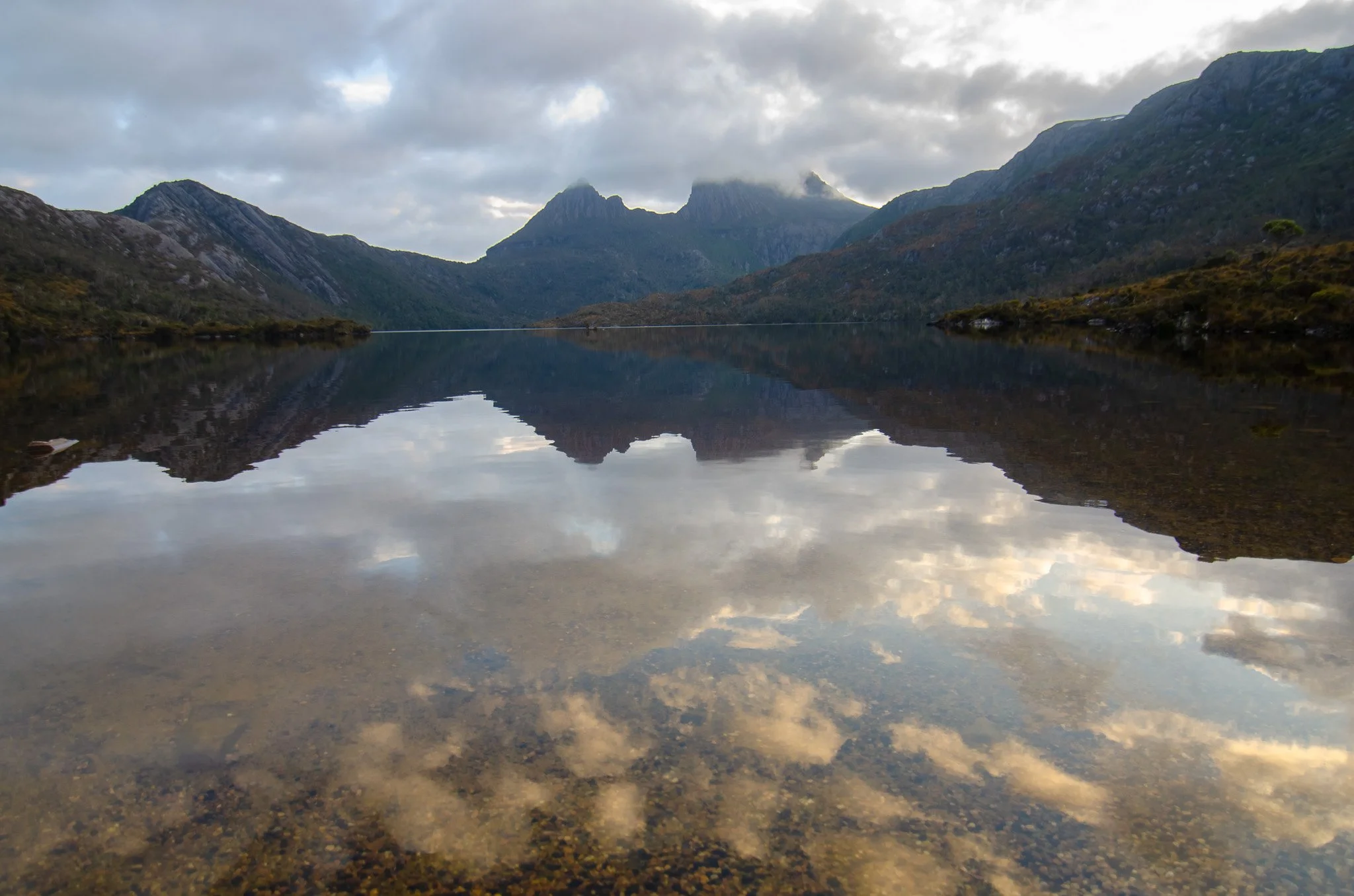 Mountain landscape with a lake reflecting the cloudy sky and surrounding mountains.