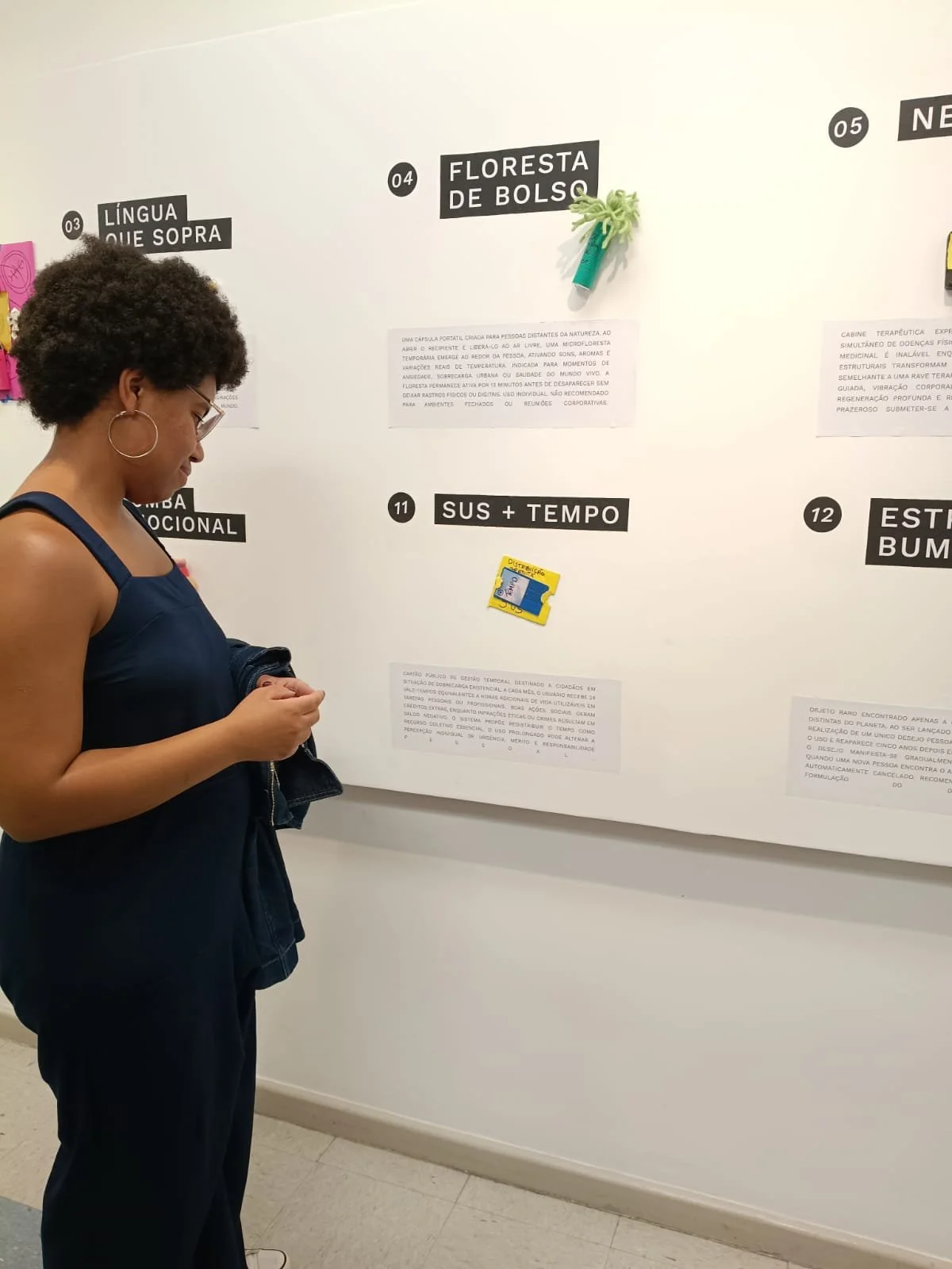 Mulher com cabelo cacheado e óculos observando uma parede com painéis de informações na exposição.