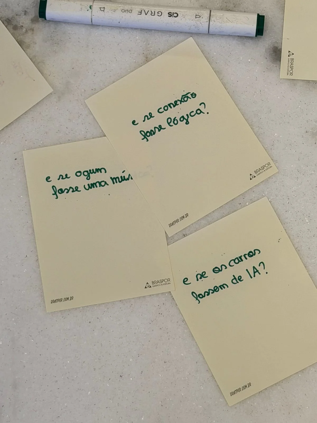 Post-its com perguntas escritas em português, em uma mesa branca. Uma caneta marca-texto azul e verde está visível na imagem.