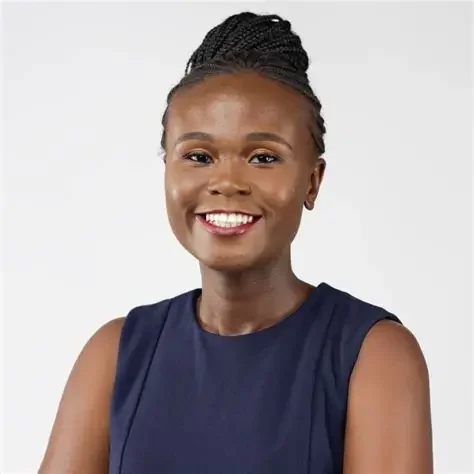 Portrait of a smiling Black woman with braided hair, wearing a sleeveless navy blue top, against a plain light background.