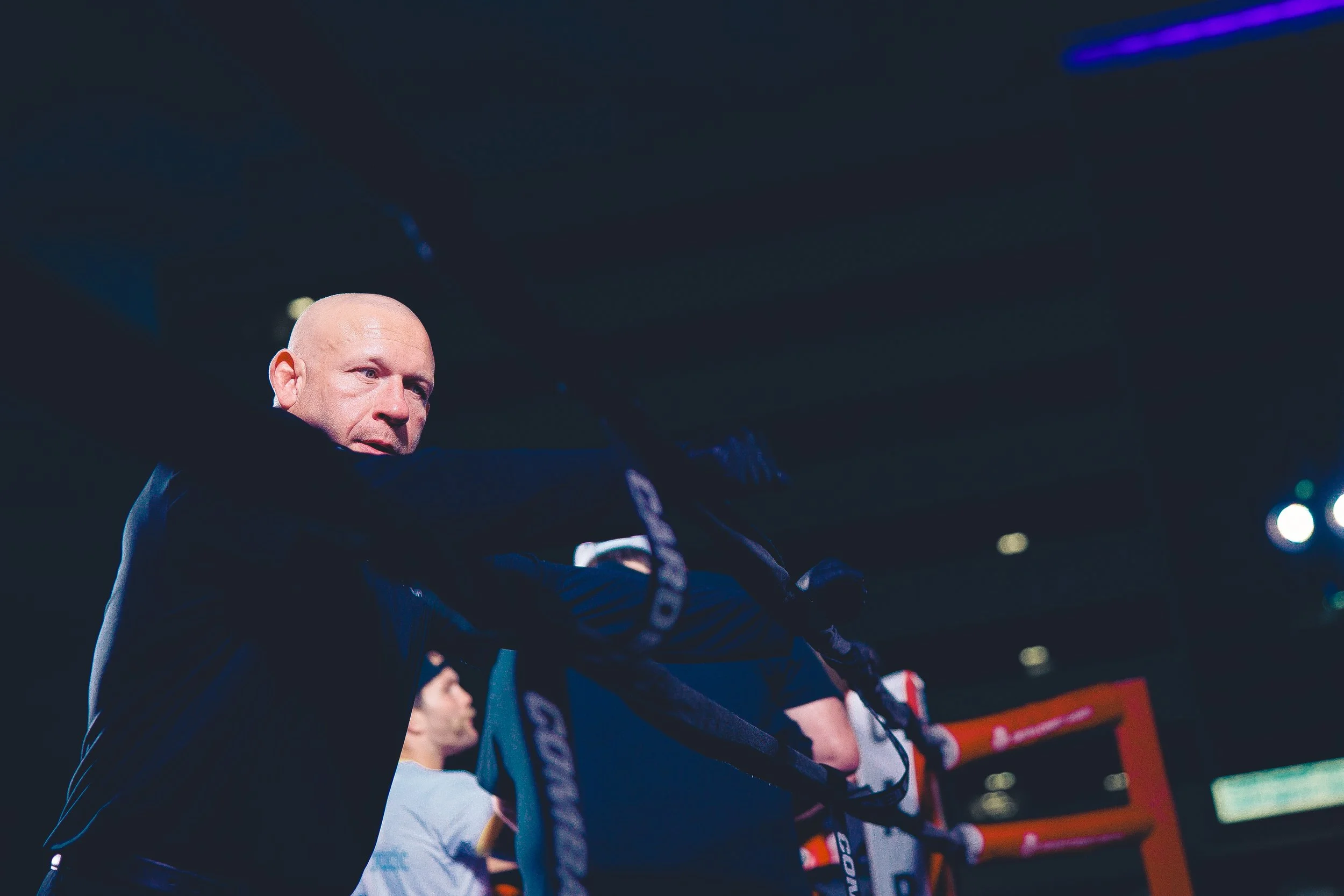 A bald man in a black suit looking over a boxing ring's ropes at an indoor event. Shot at Evergy Plaza in Topeka, Kansas. 