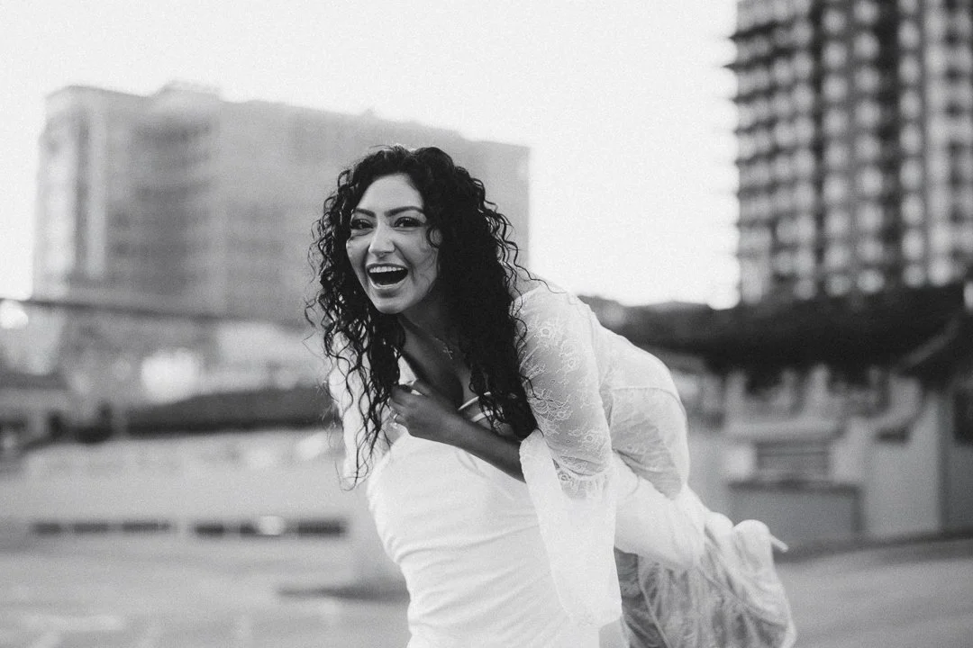 A woman with curly hair and a lace top laughing and leaning on someone's back in an urban rooftop setting. Shot at Kansas City, Country Club Plaza.