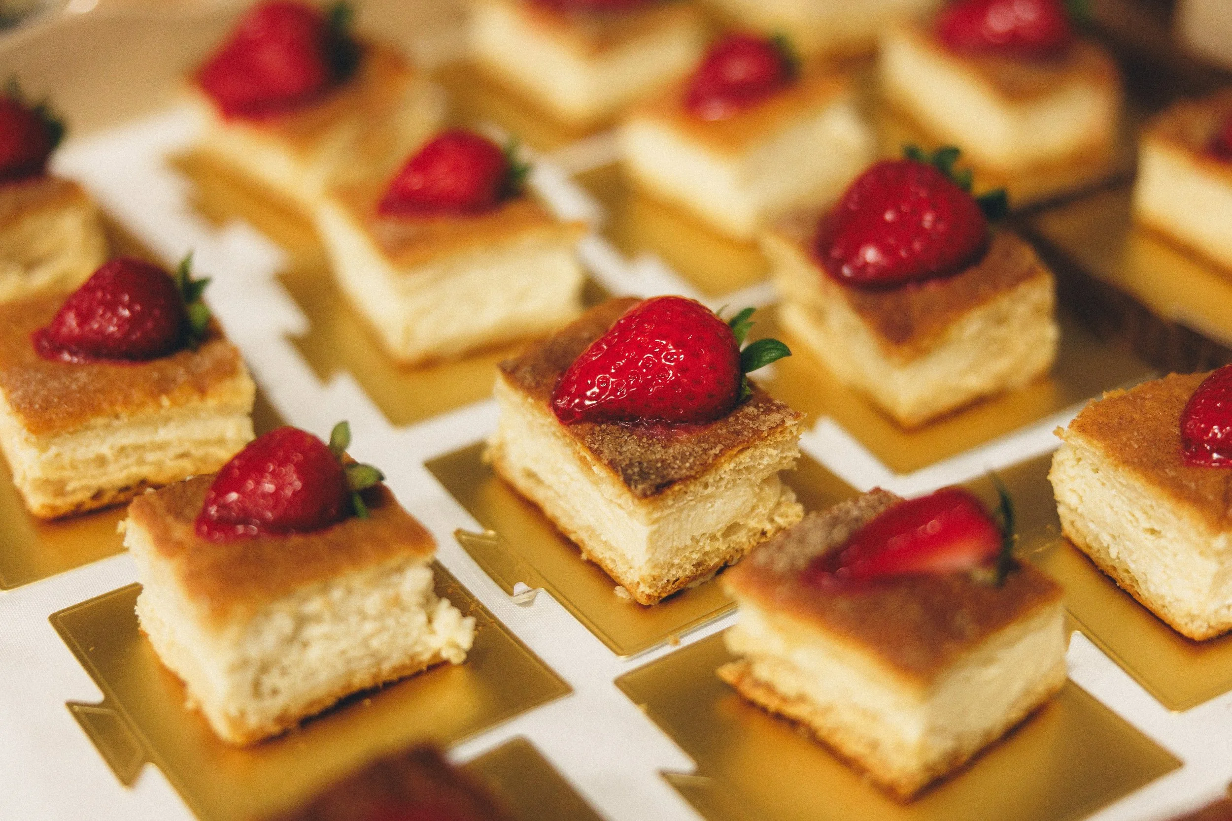 Small square pieces of cake topped with strawberries on a gold tray.