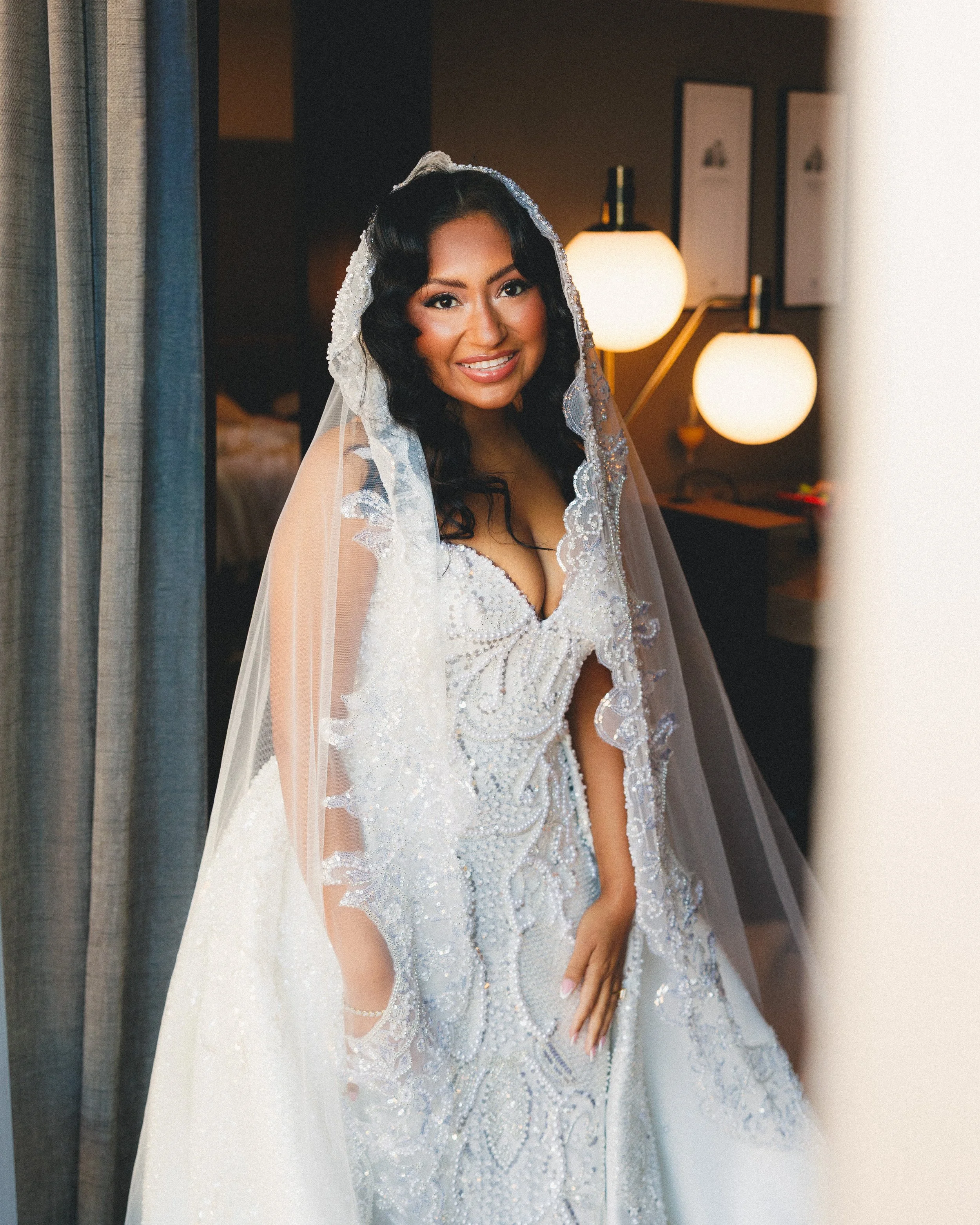 A woman in a wedding dress with a veil, smiling in a warmly lit indoor setting. Shot at Cyrus Hotel in Topeka, Kansas.