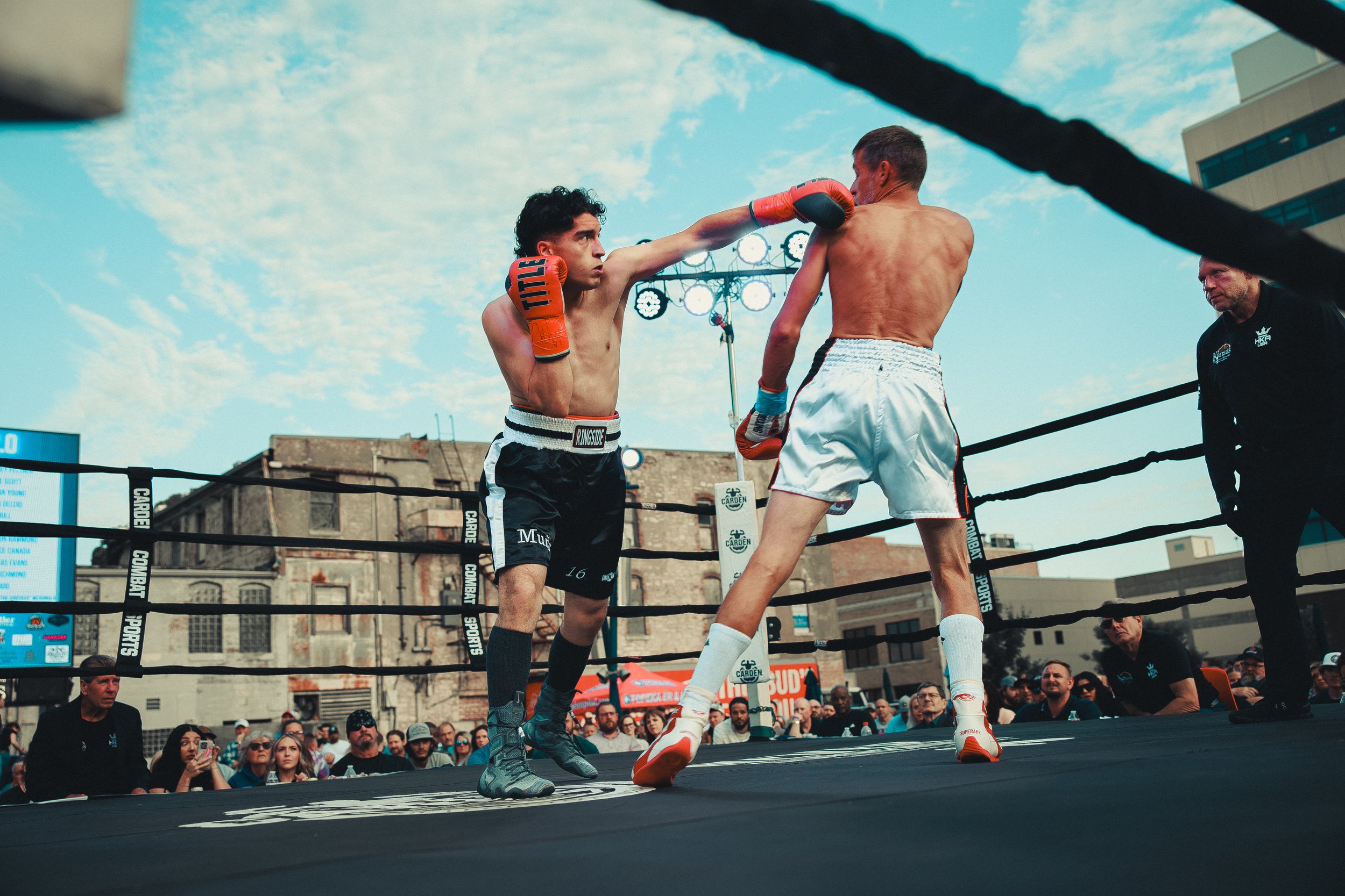 Two amateur boxers sparring in an outdoor ring with a crowd watching, one punch connected to the other boxer's face. Shot at Evergy Plaza in Topeka, Kansas. 