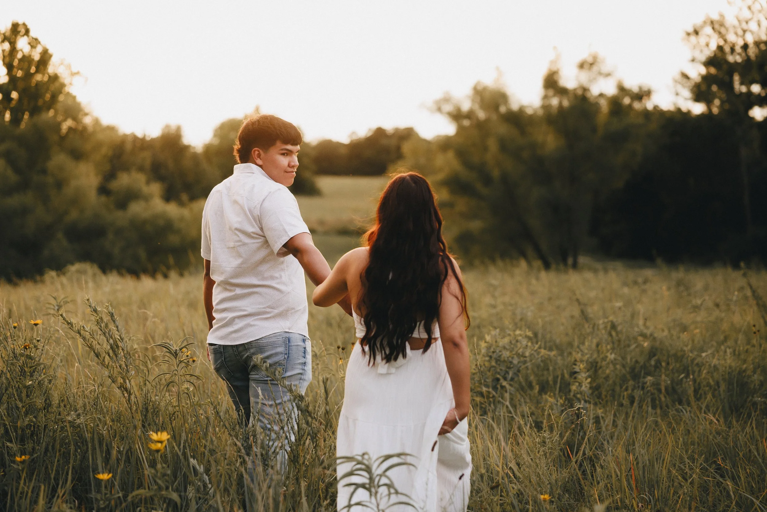 A young man helps a woman walk through a grassy field during sunset, surrounded by trees.  Shot in Topeka, Kansas. 