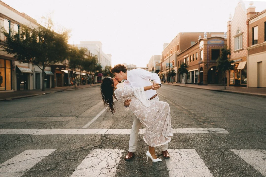 A couple dancing and kissing in the middle of a street at sunset, with empty shops and buildings on both sides. Shot at Kansas City, Country Club Plaza.