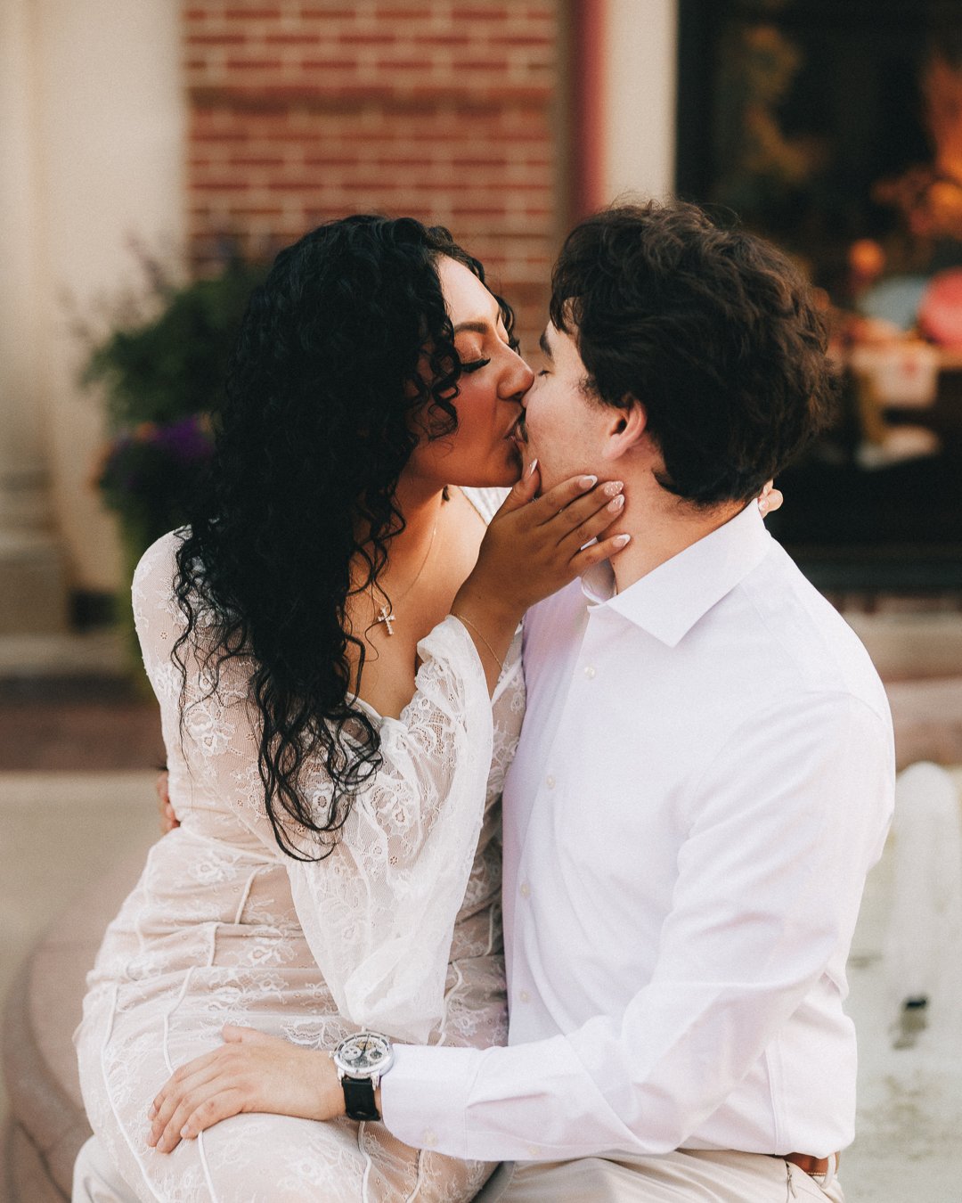 A couple kissing intimately inside a cozy room with a brick wall and decorative lights in the background. Shot at Kansas City, Country Club Plaza.