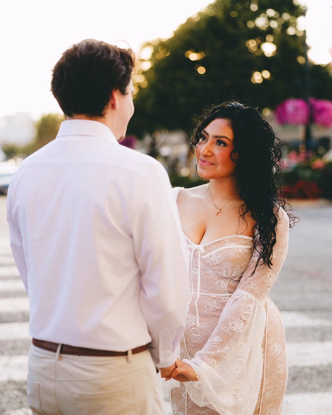 A woman in a sheer lace dress holding hands with a man in a white shirt outdoors at sunset. Shot at Kansas City, Country Club Plaza.