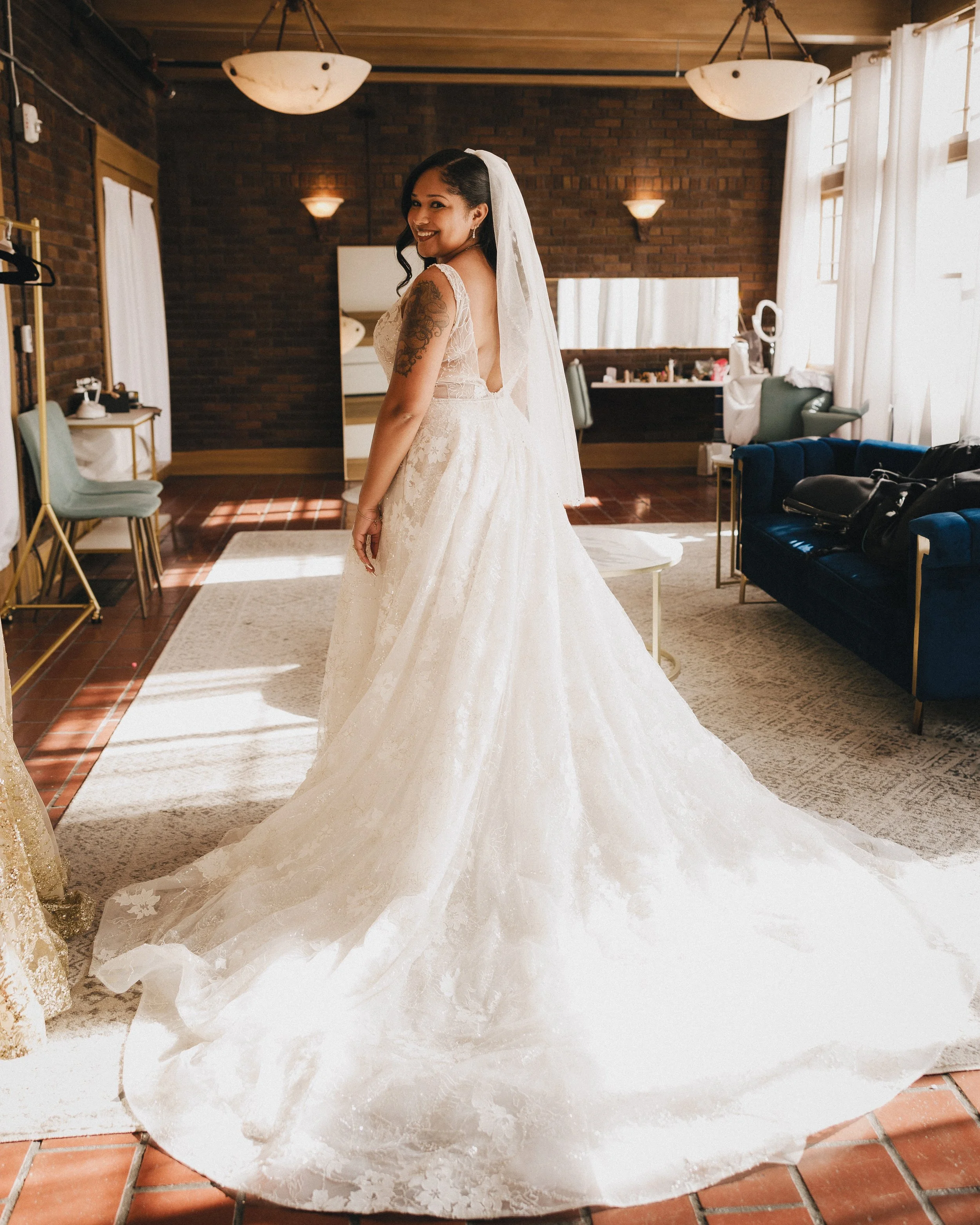 A woman in a wedding dress standing in a well-lit room with brick walls, smiling at the camera. Shot at Topeka Kansas venue The Beacon.