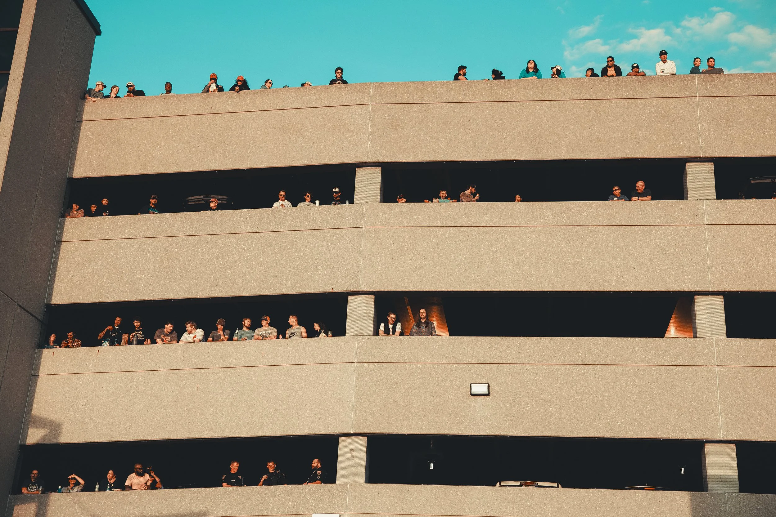 People gathered on different levels of a parking garage, overlooking the street under a blue sky. Shot at Evergy Plaza in Topeka, Kansas. 