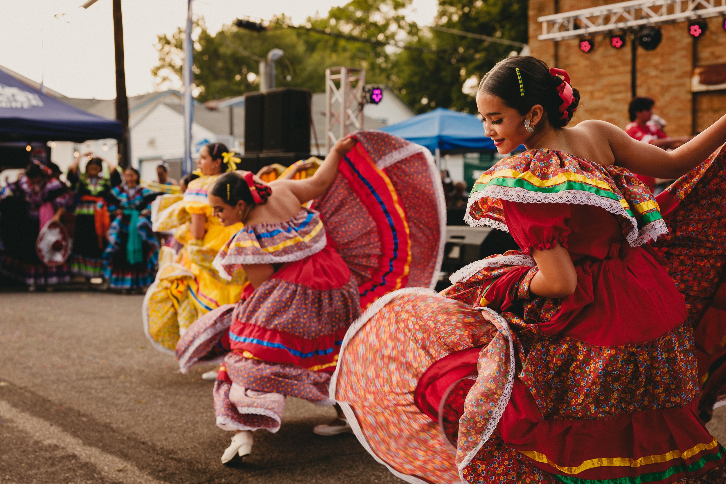 Young women in colorful traditional Mexican dresses dancing outdoors during a cultural celebration. Shot at Fiesta Topeka. 