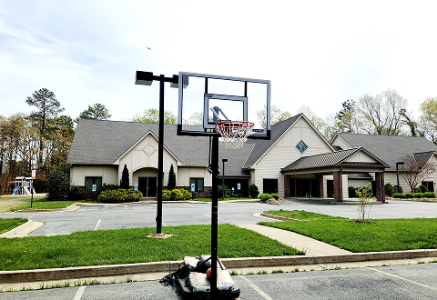 An empty outdoor basketball hoop, with our church in the background.
