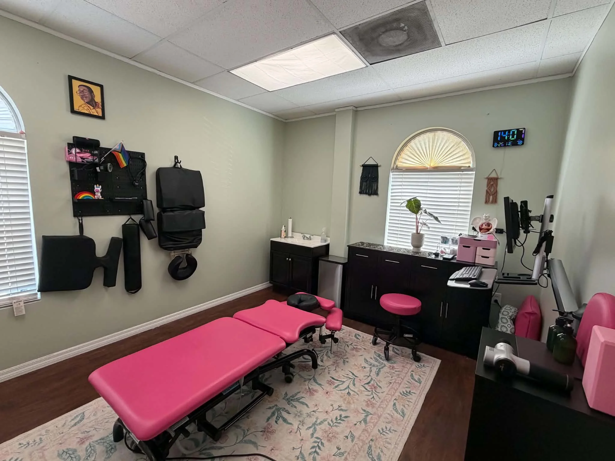 Medical or therapy treatment room with pink therapy beds, a computer station, and healing decor on the walls.