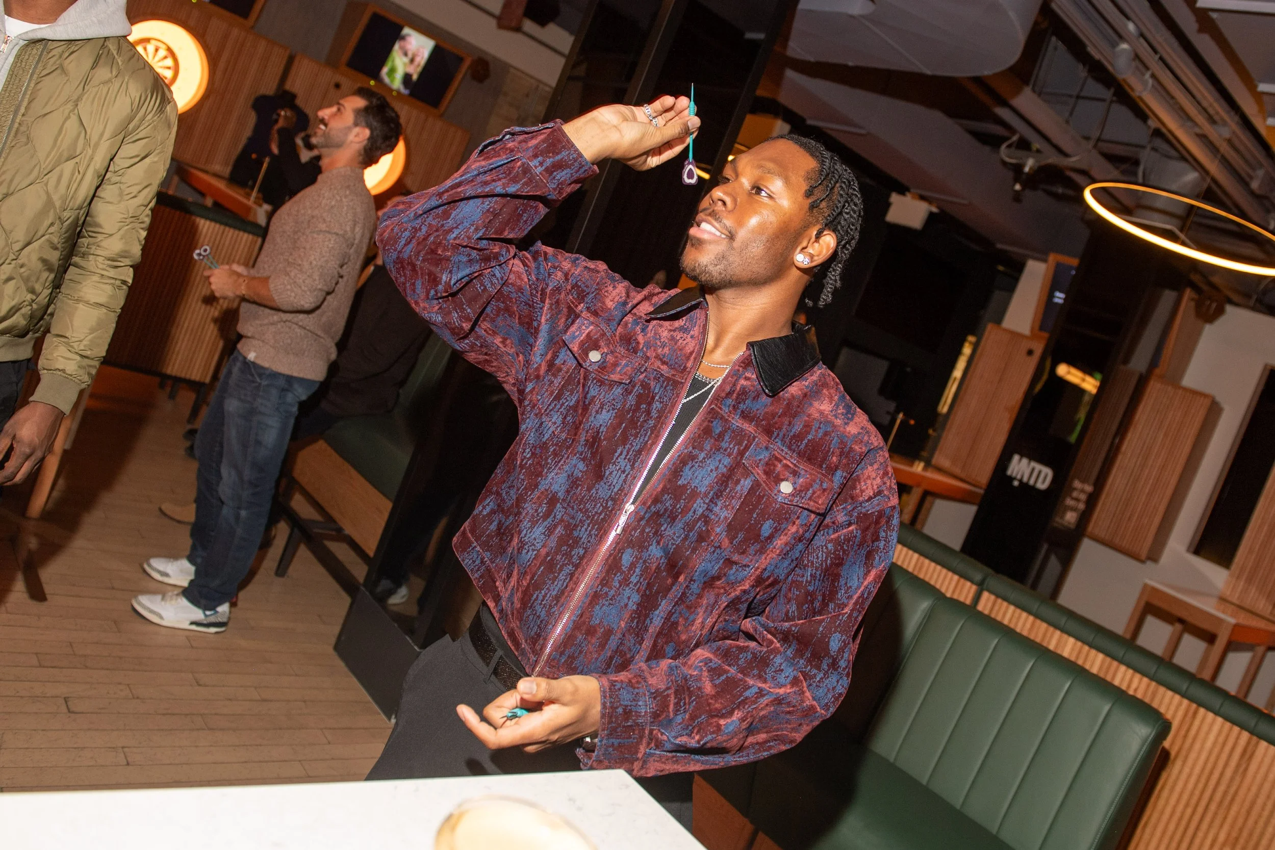 An action photo of a VIP guest at the MNTD launch event hosted by Public/Realm; the guest is in the midst of throwing a dart at a dart board out of frame