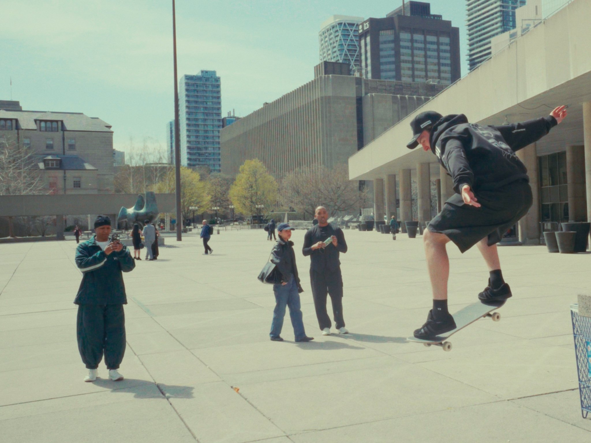 Behind-the-scenes footage of a professional skateboarder performing tricks in the park while another tastemaker captures the footage during the fashion film shoot.