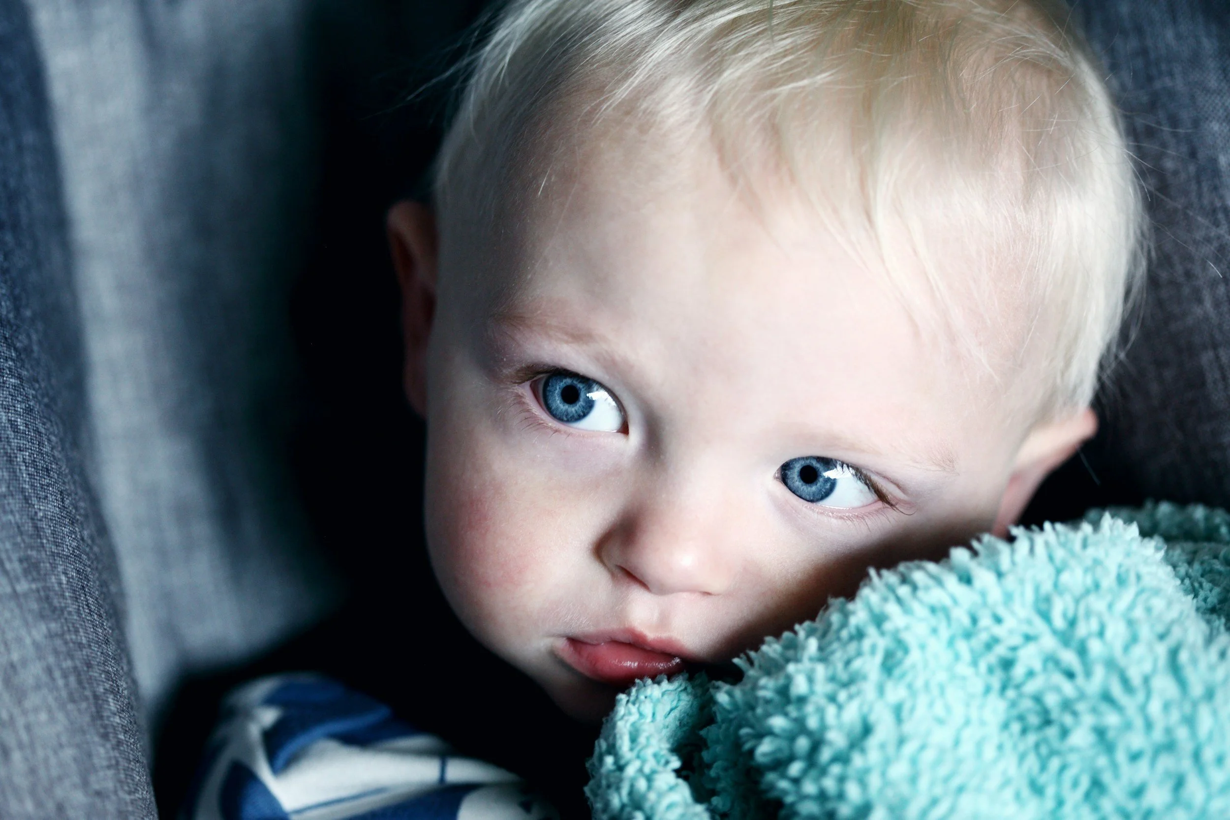 Young blonde-haired child with blue eyes looking sideways while resting on a soft blue-green blanket.