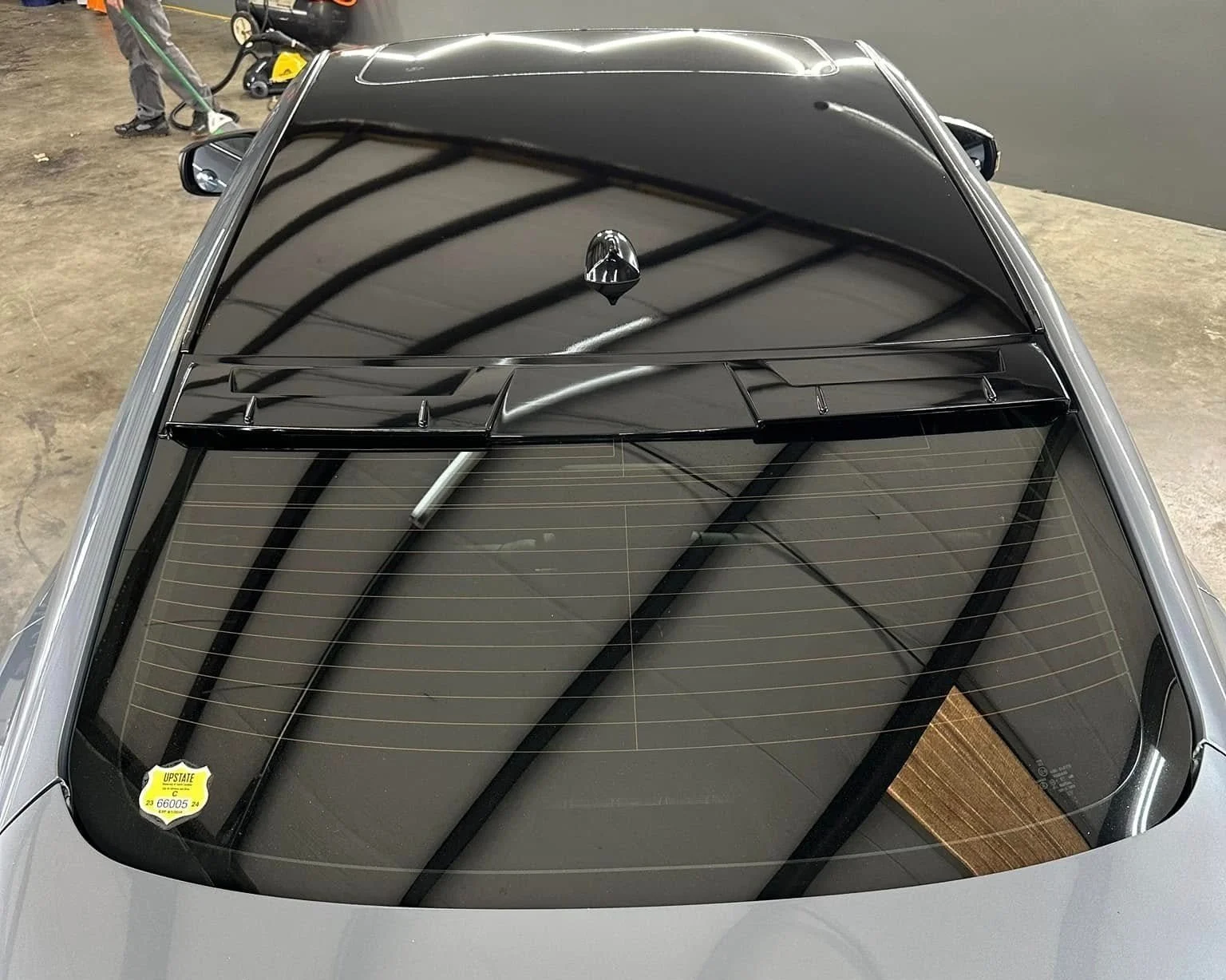 Top view of a silver car with a black roof and rear window, reflecting the ceiling structure of a garage or warehouse.