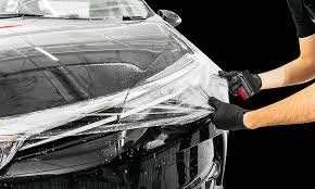 A person applying a protective film or wrap to the front of a black car.