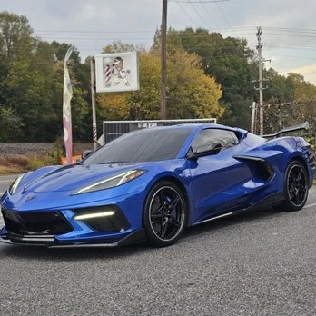 Blue sports car parked on the side of the road with trees and utility poles in the background.