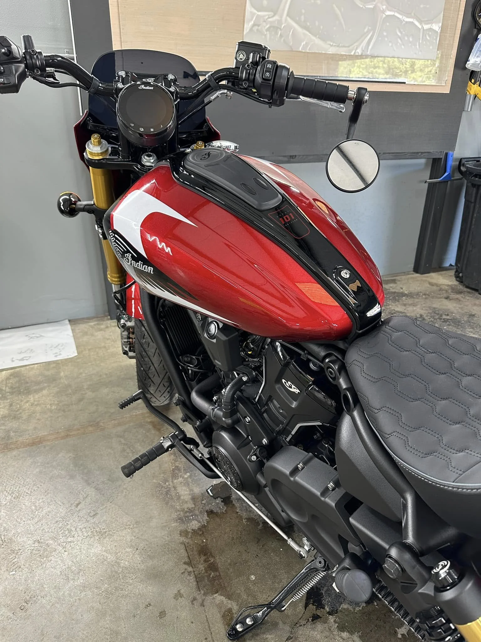 Red and black Indian Scout motorcycle in a garage with a concrete floor and gray walls.