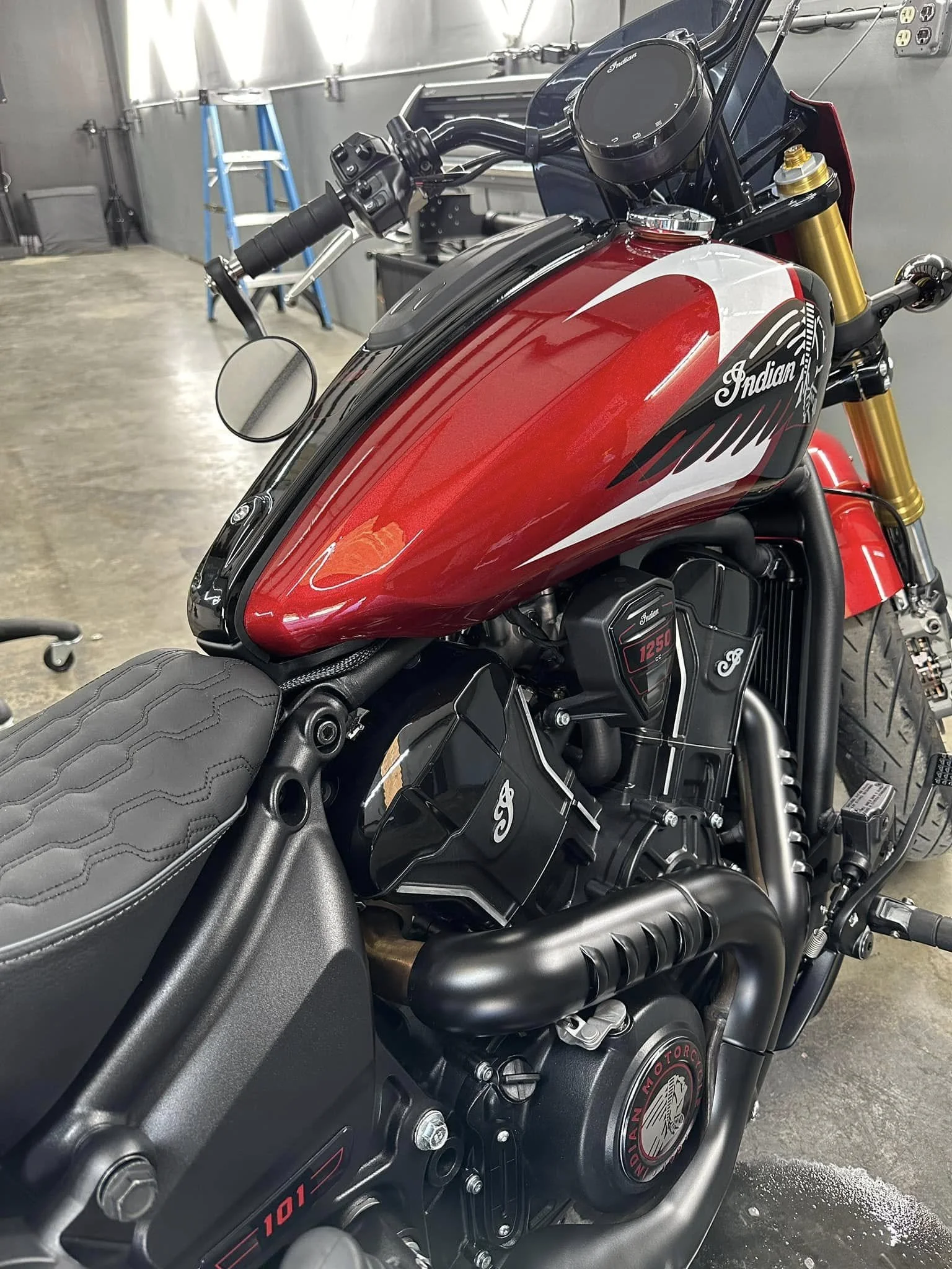 Close-up of a red and black Indian Motorcycle with a black seat, gold front forks, and visible engine components in a garage.