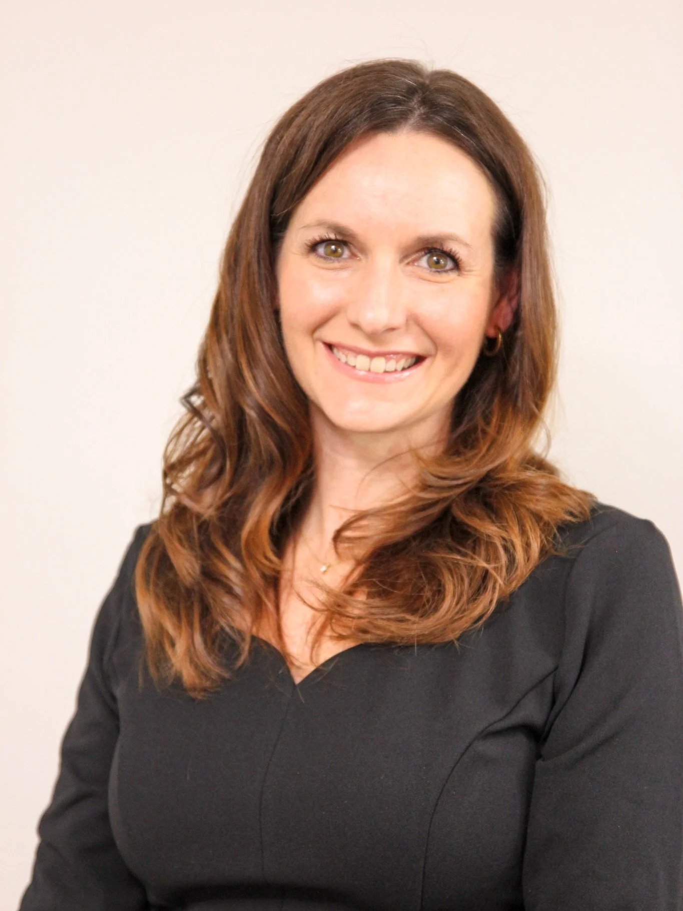 Smiling woman with long brown hair wearing a black shirt against a gray background.