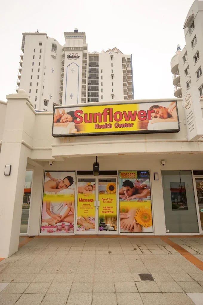 Outside view of massage shop Sunflower Health Centre in Broadbeach with yellow themed flower and massage scenes stickered across windows and doors and large lightbox signage above.
