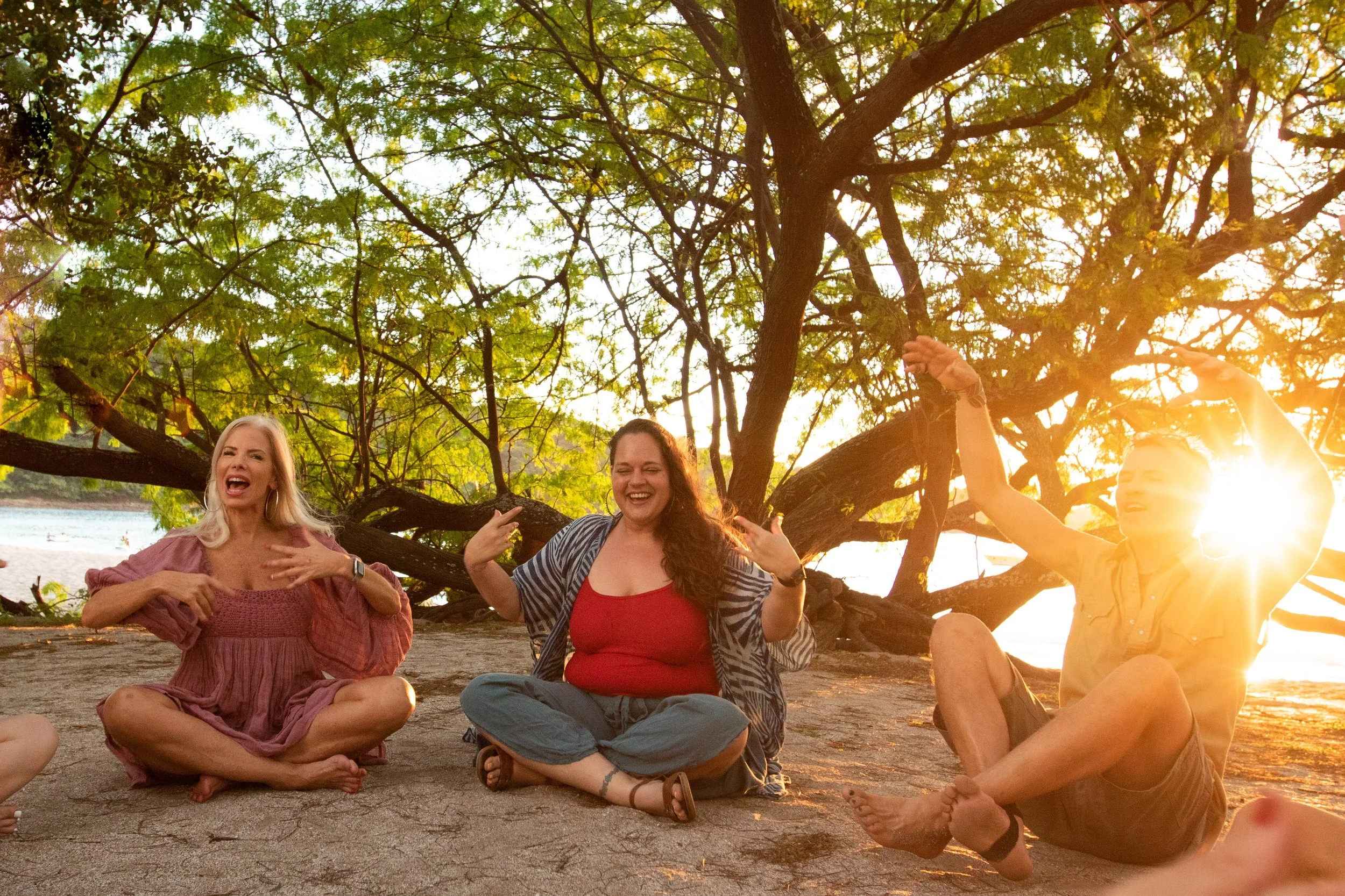 A group of people sitting on the ground near a tree, laughing and enjoying each other's company during sunset.