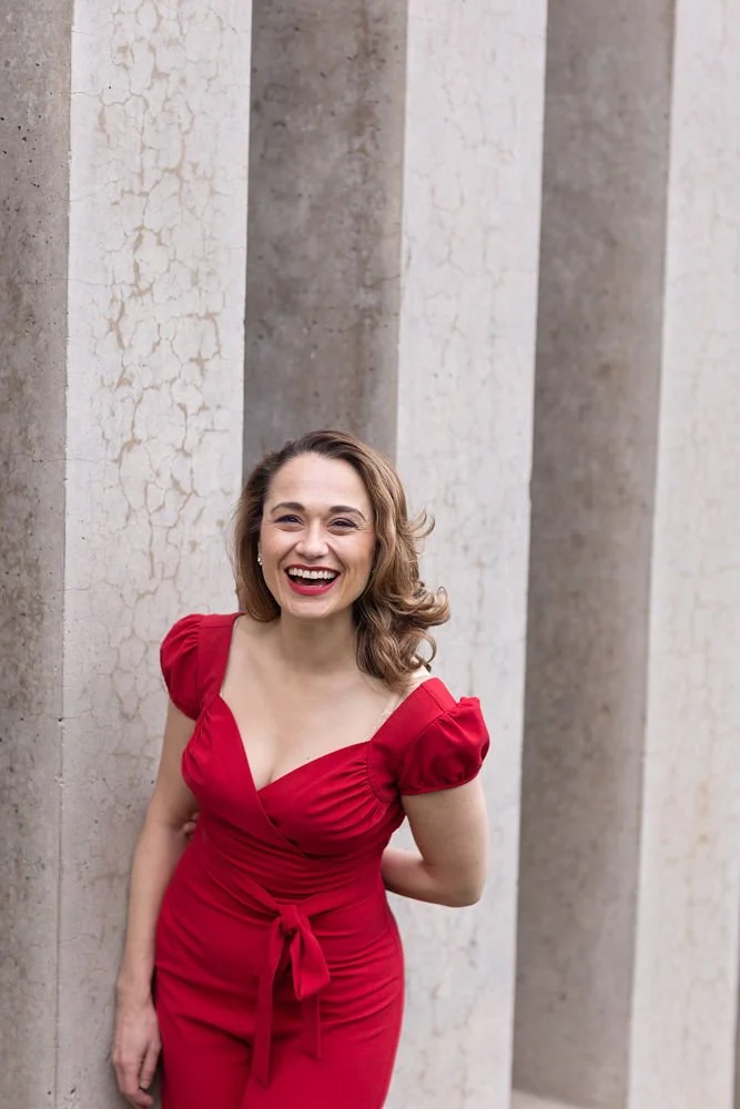 Woman in red dress laughing and standing against concrete columns.