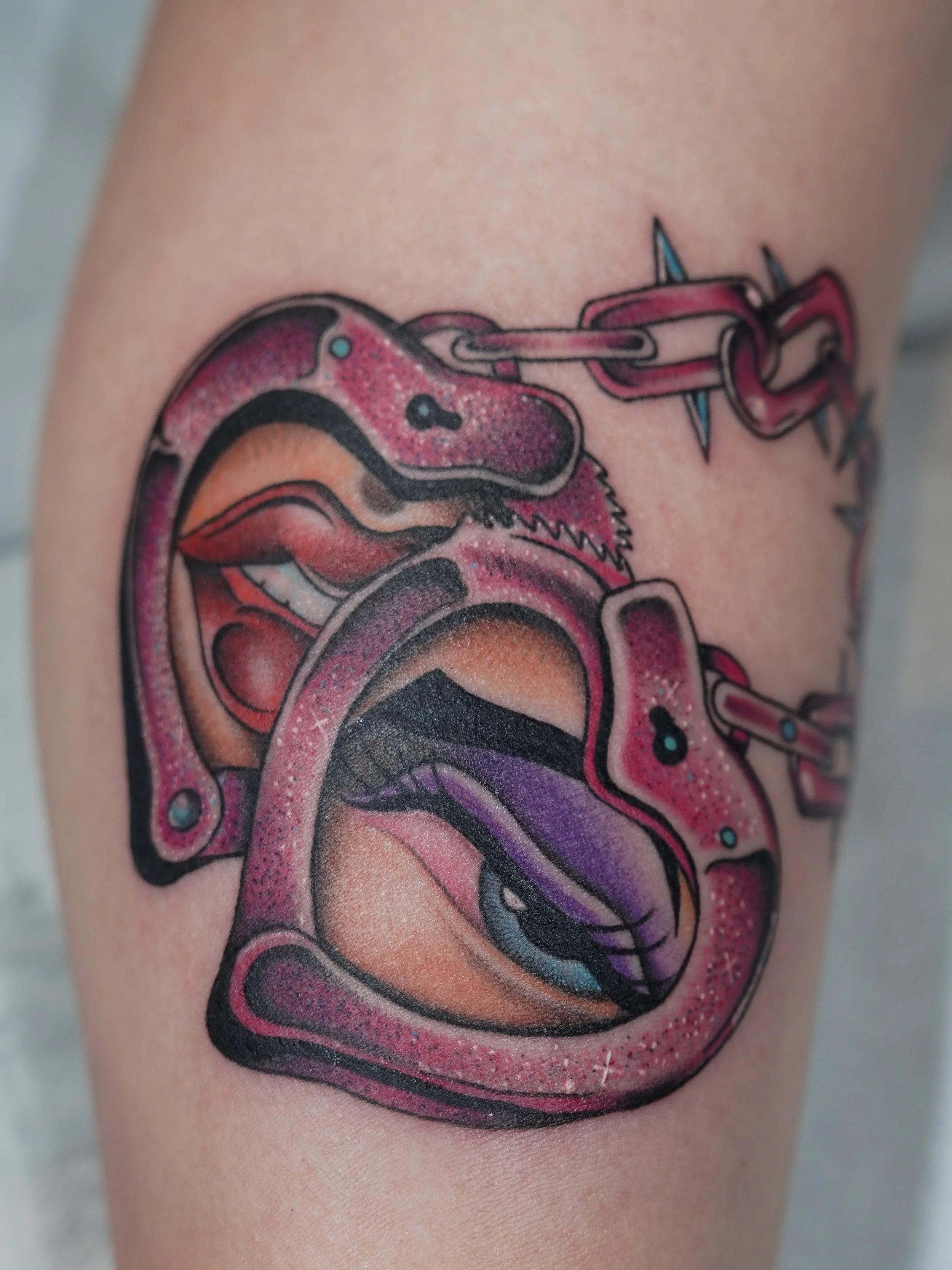 Close-up of a colorful tattoo on skin, depicting a stylized snake intertwined with other shapes, using pink, purple, black, and teal ink.