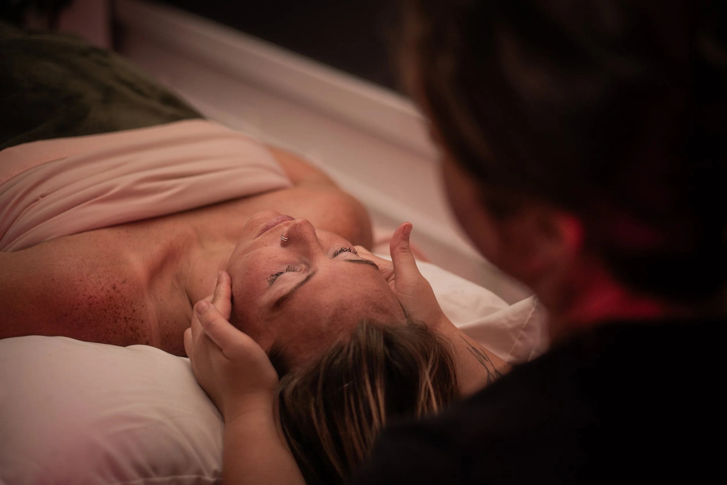 A person receiving a forehead massage from another person lying on a bed, with their eyes closed.