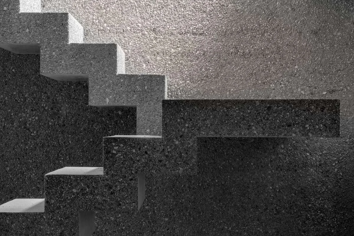 A modern staircase with dark, textured steps, leading upward against a light background. The stairs have a minimalist design with no railing.