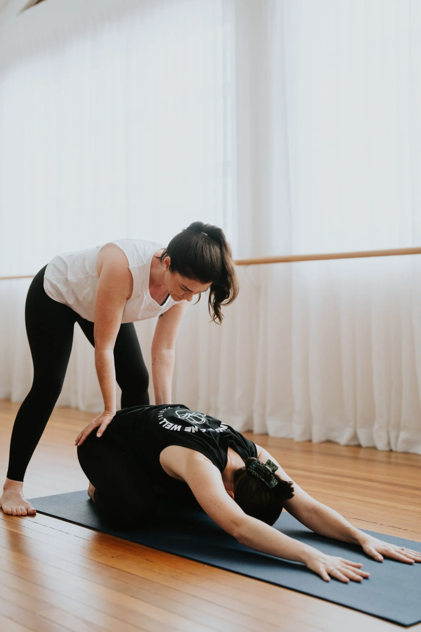 An instructor puts gentle pressure on a person's back at a mat yoga class at Antara Studios