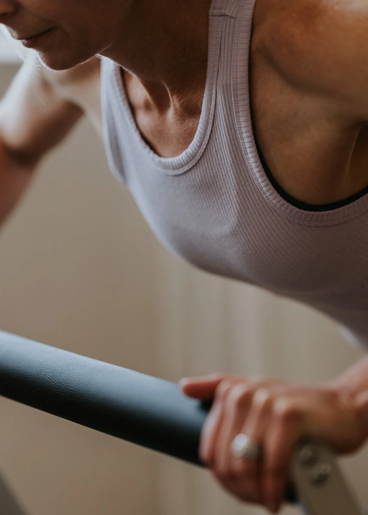 Close-up of a person wearing a white tank top, gripping a horizontal bar during a reformer Pilates class.